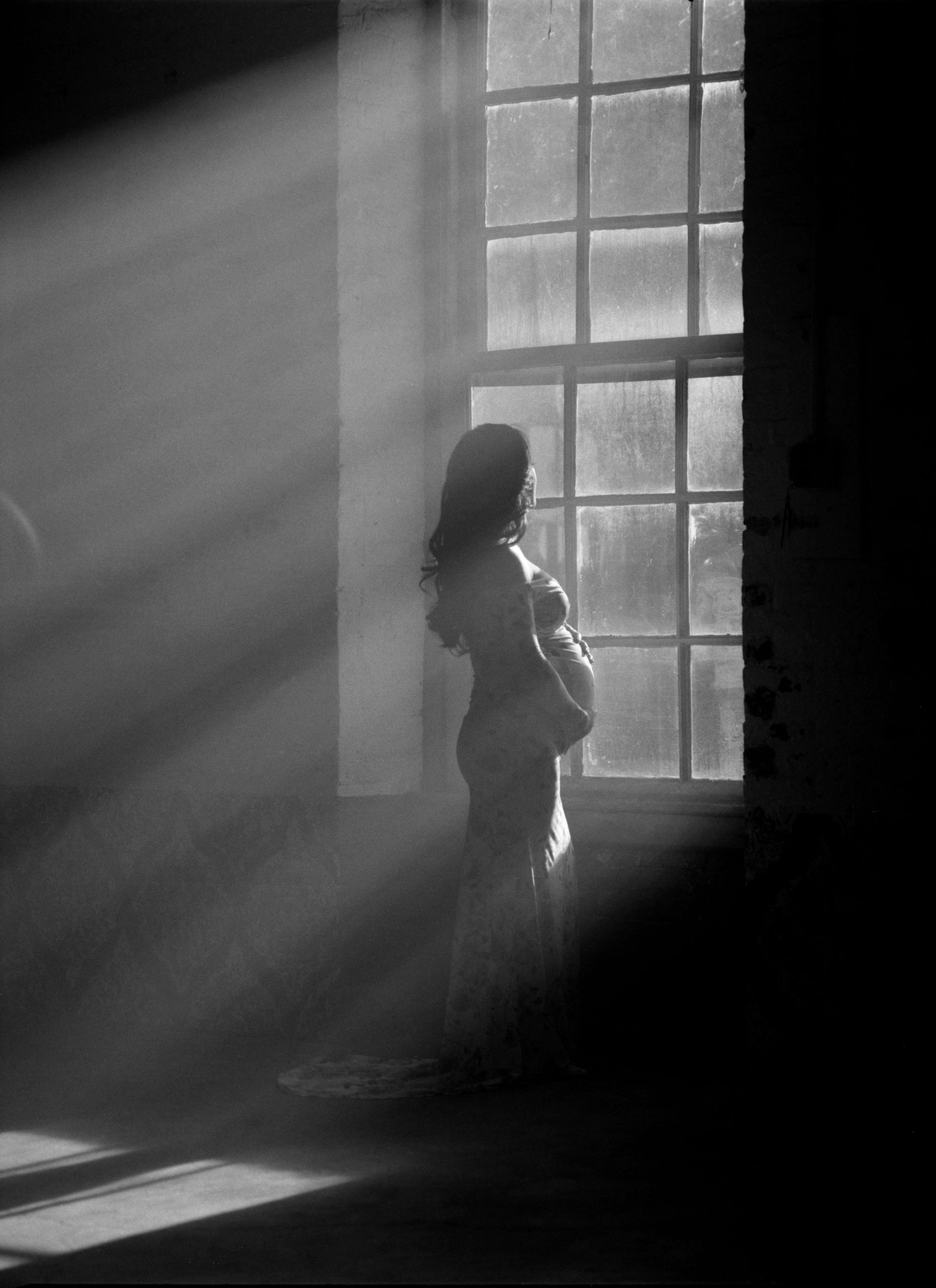A black and white photo of a woman looking out a window