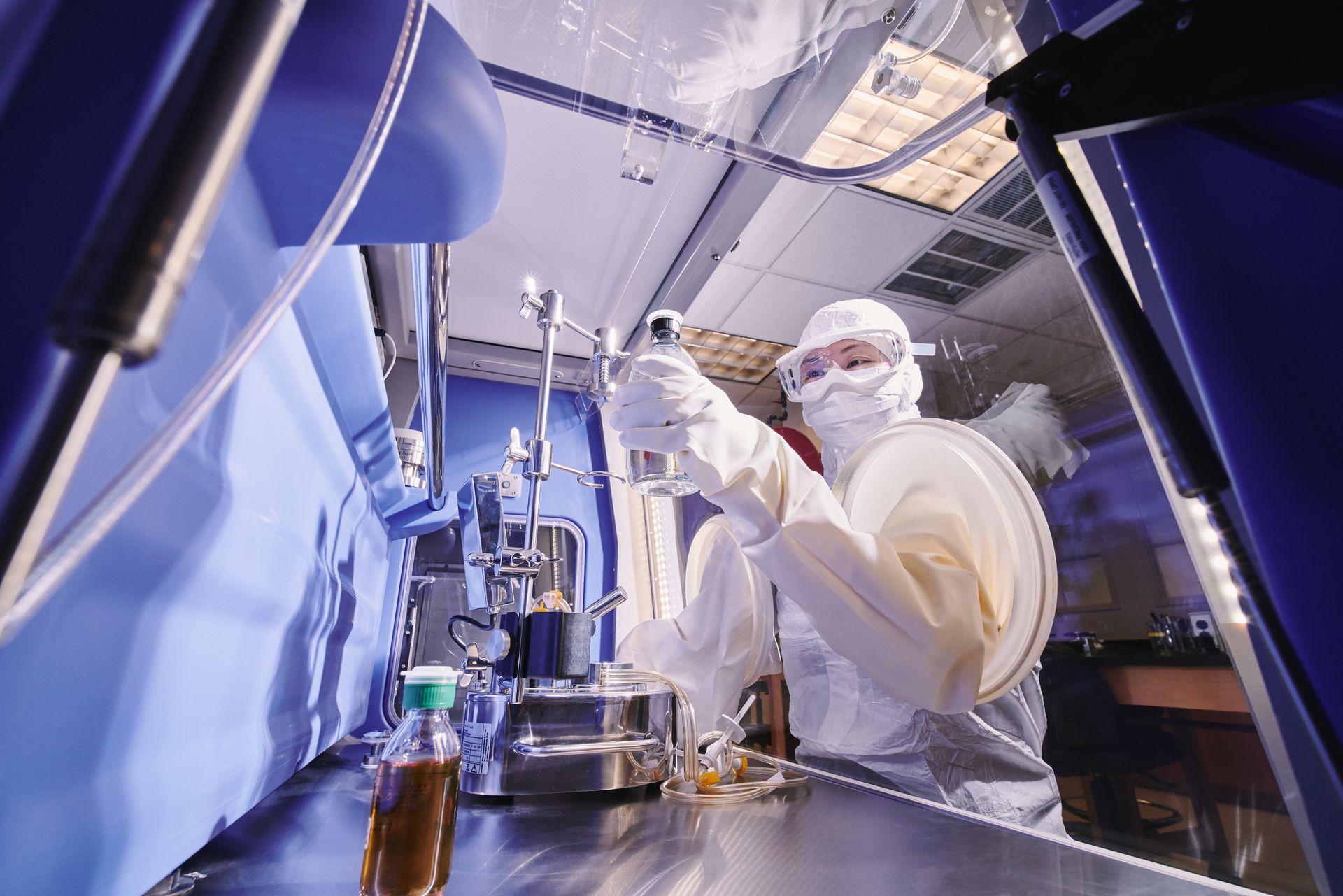 Scientist in protective gear working in a lab with machinery, blue and steel setting.