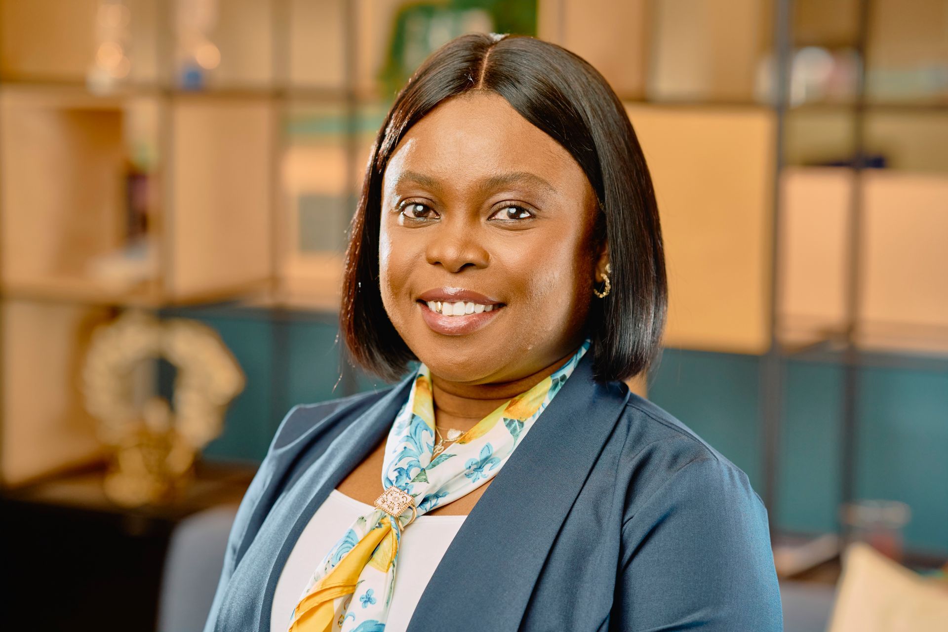Smiling professional in a blue blazer and patterned scarf seated in a modern office