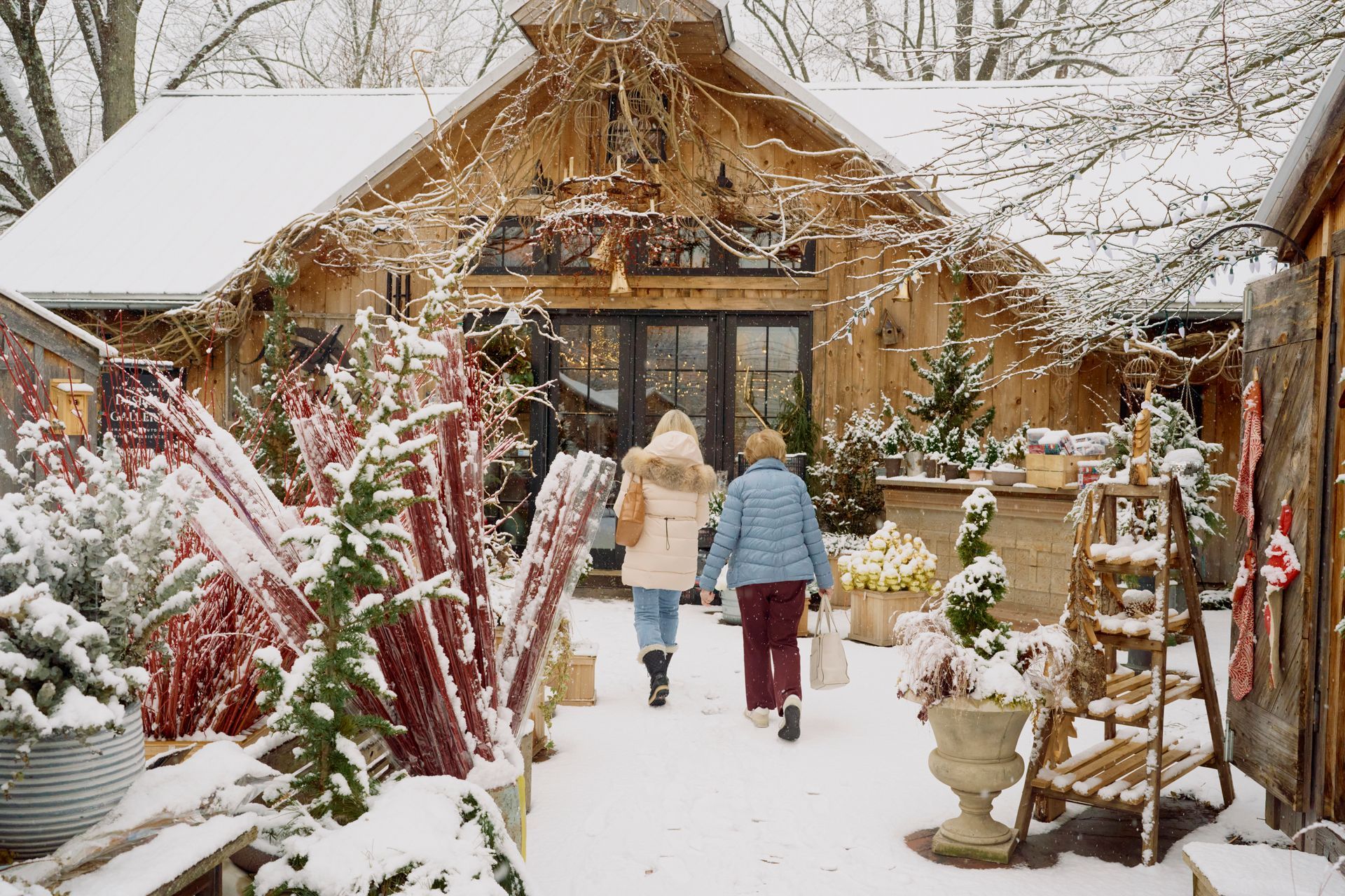 Two people walking towards a snow-covered wooden building decorated with lights and winter greenery.