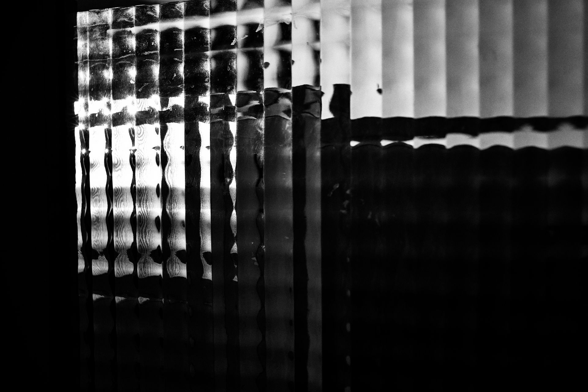 Textured glass panel reflects light, casting shadows. Dark setting, geometric shapes.