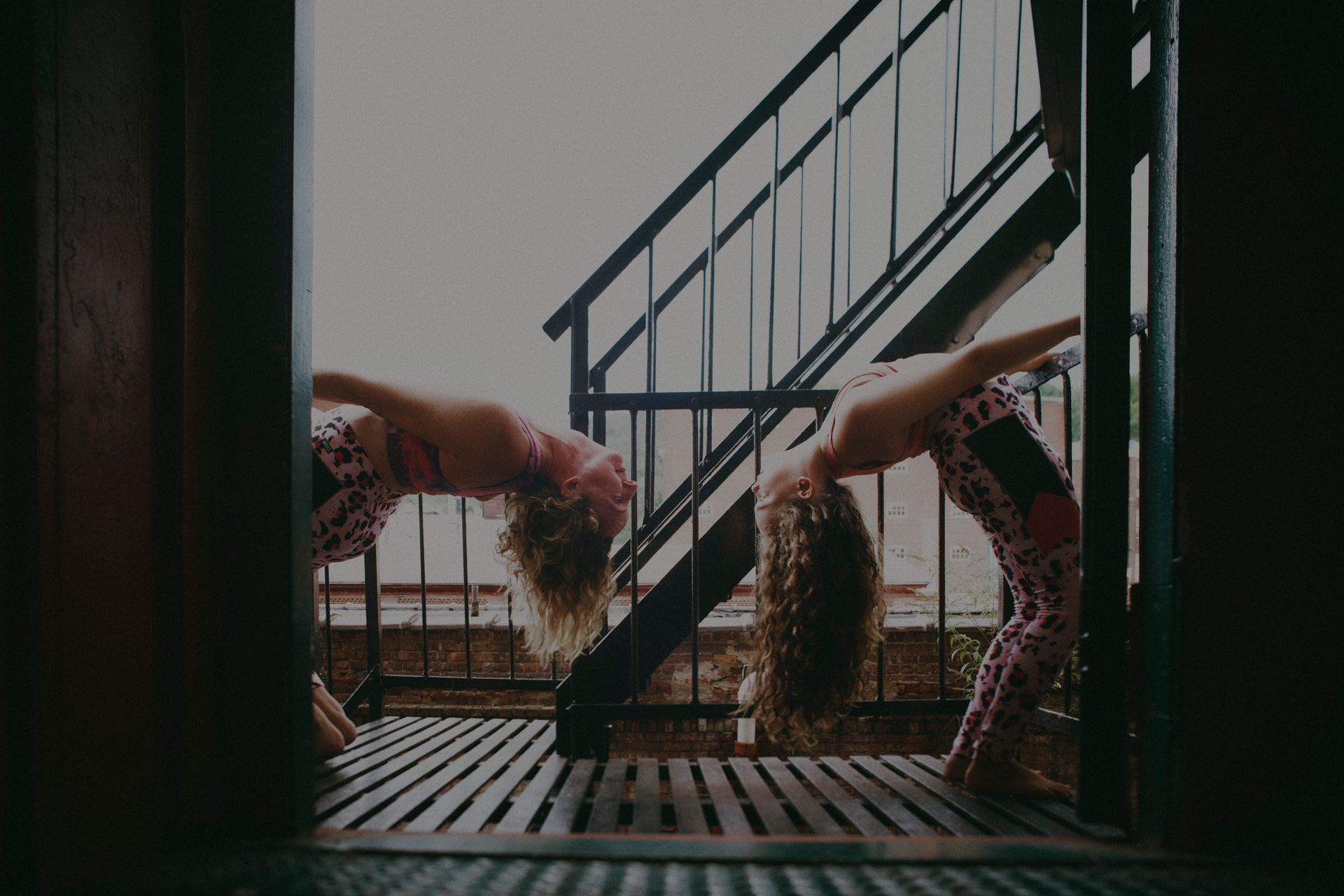 Two people doing yoga on a rooftop deck beside a metal staircase at sunset