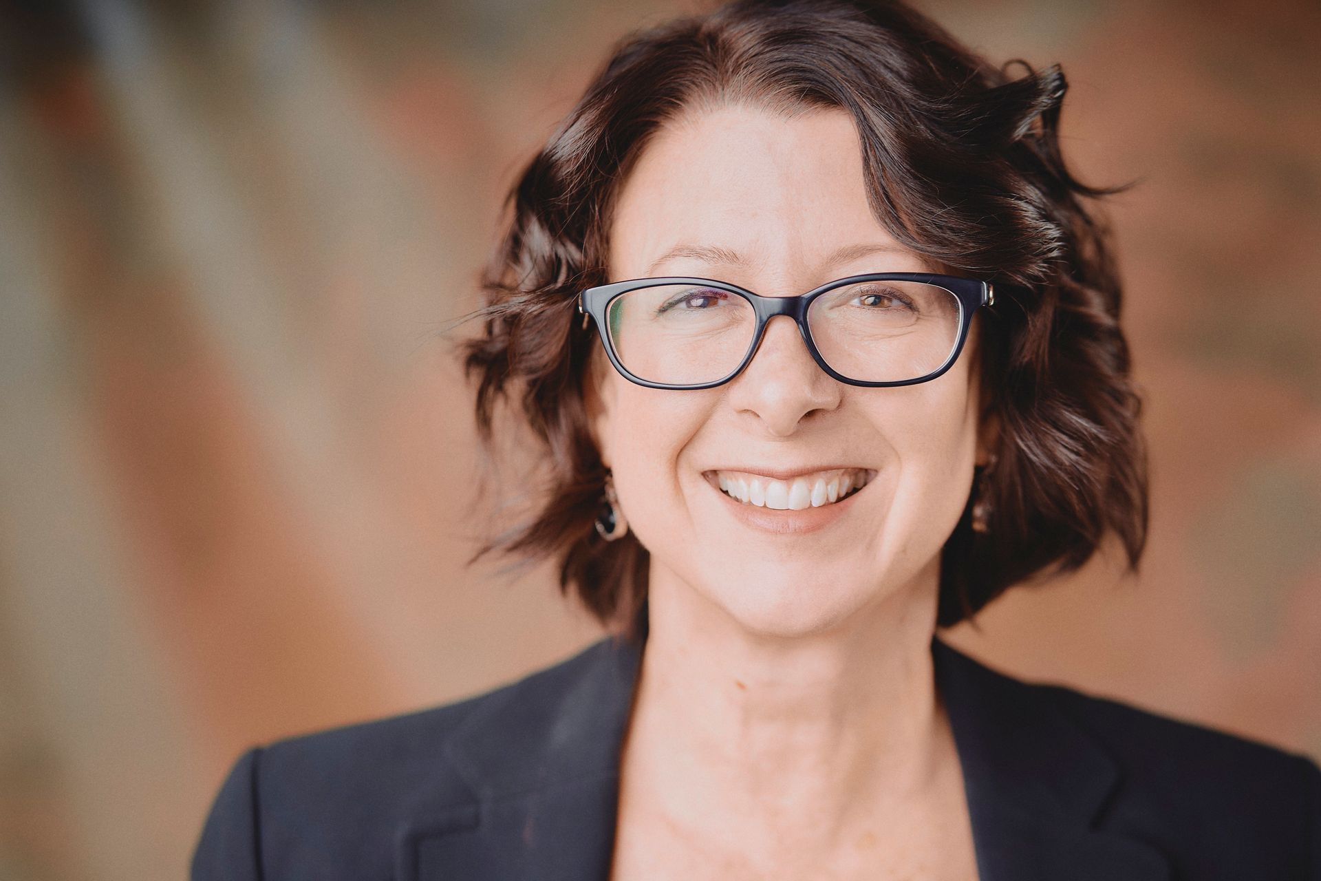 A woman wearing glasses and a black jacket is smiling for the camera.