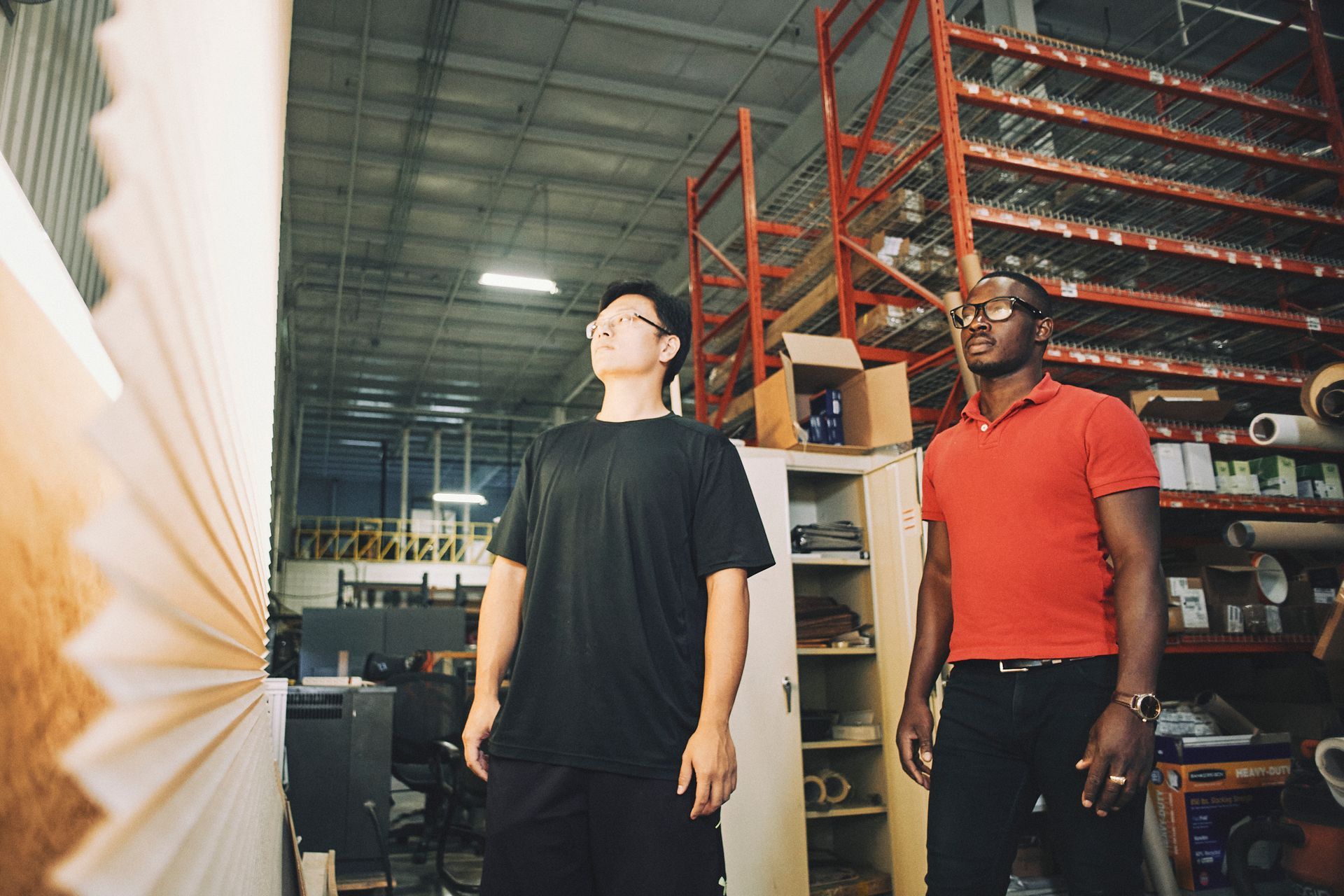 Two men are standing in a warehouse looking up at something.