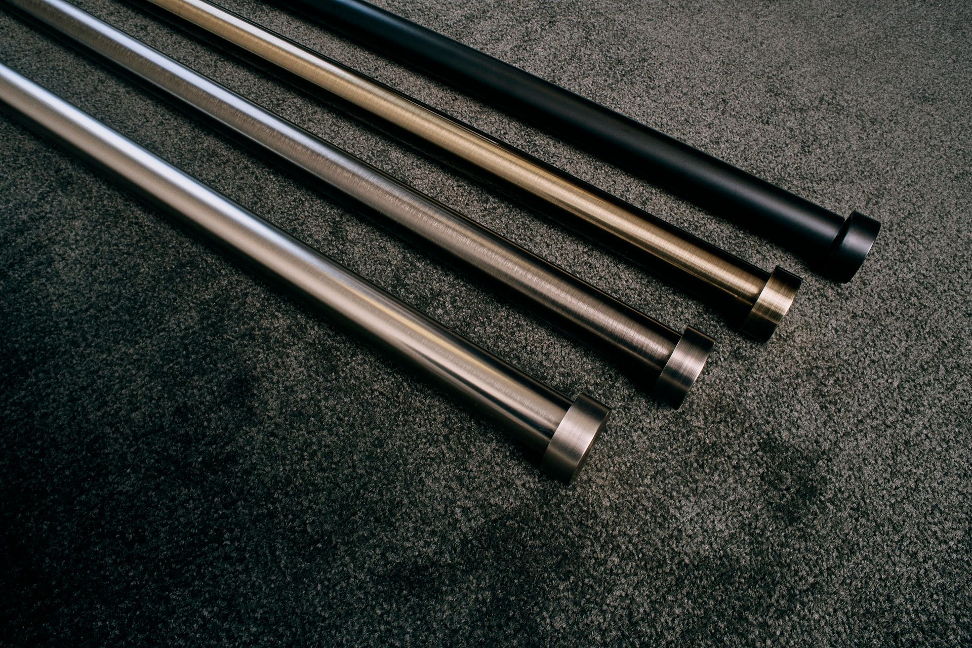 Four metal poles of different colors are sitting on a carpet.