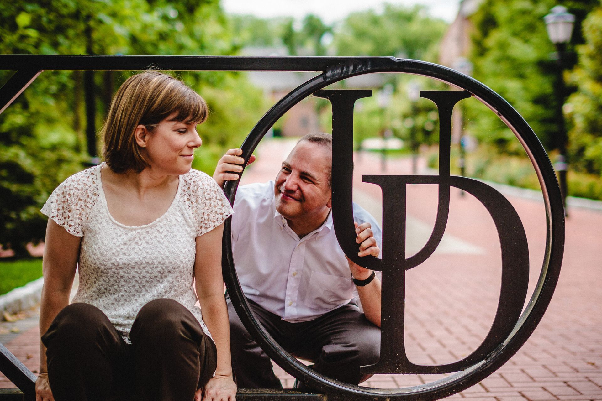 Couple smiles near a decorative metal gate with large letters outdoors.