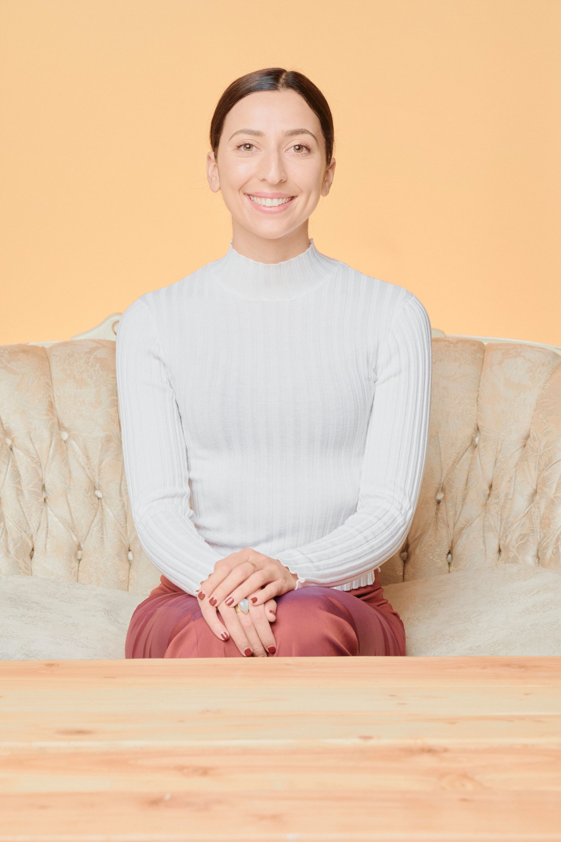 A woman is sitting on a couch with her legs crossed and smiling.