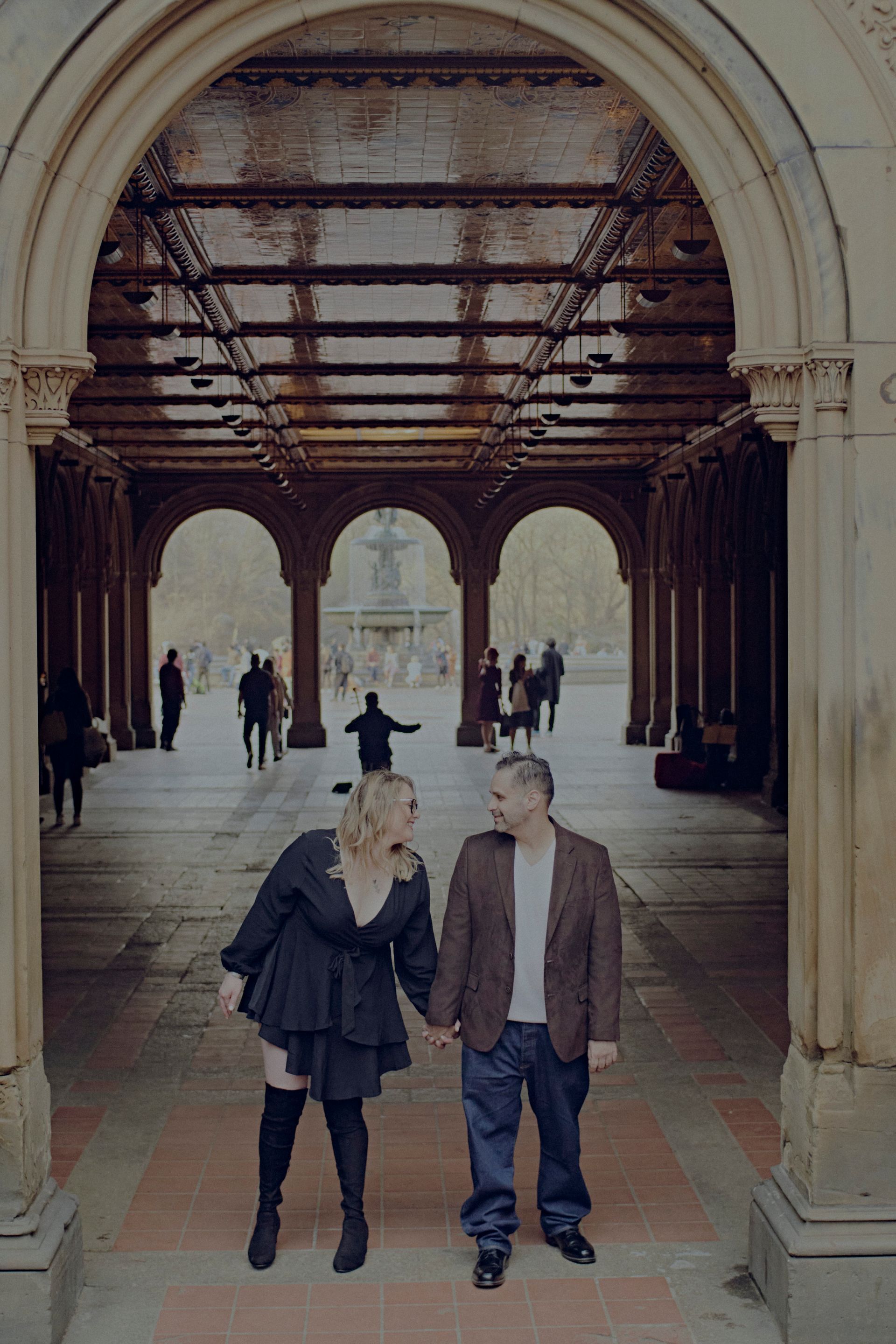 A man and a woman are holding hands under an archway in a park.