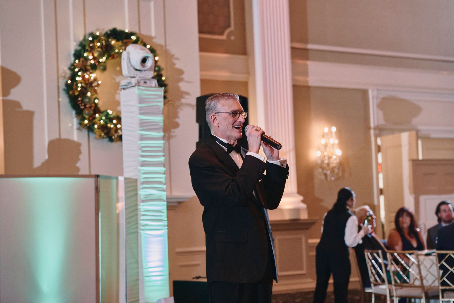 A man in a suit is singing into a microphone at a wedding reception.