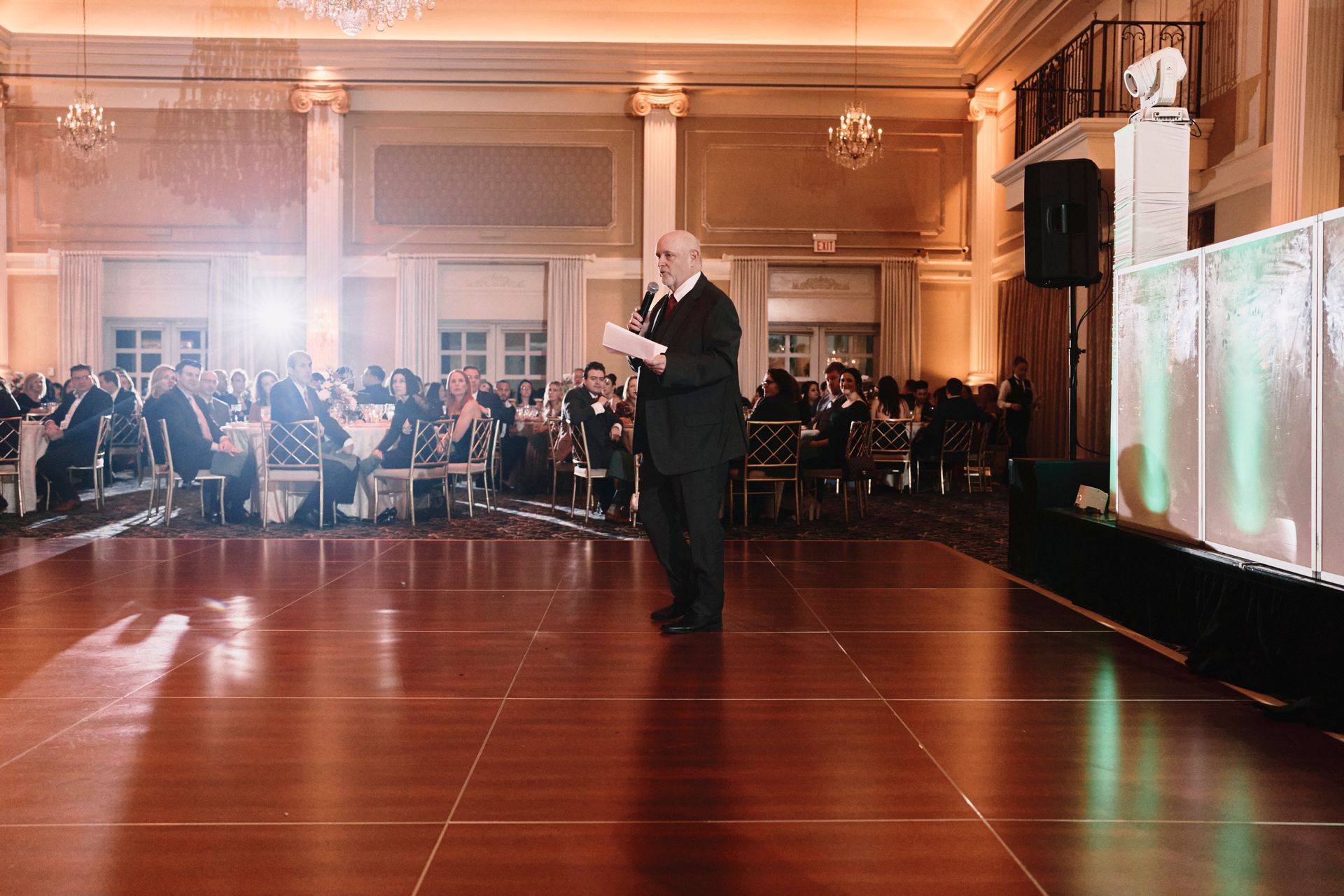 A man is standing on a dance floor giving a speech.