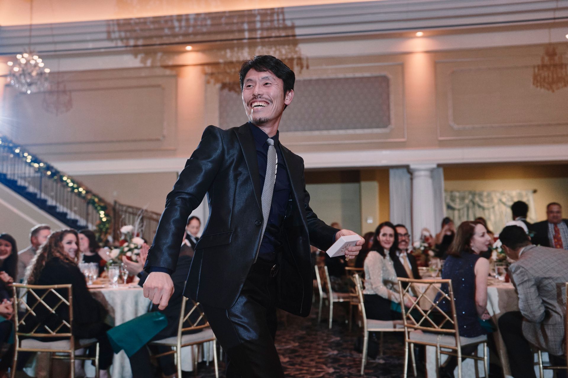A man in a suit is dancing in front of a crowd of people at a wedding reception.