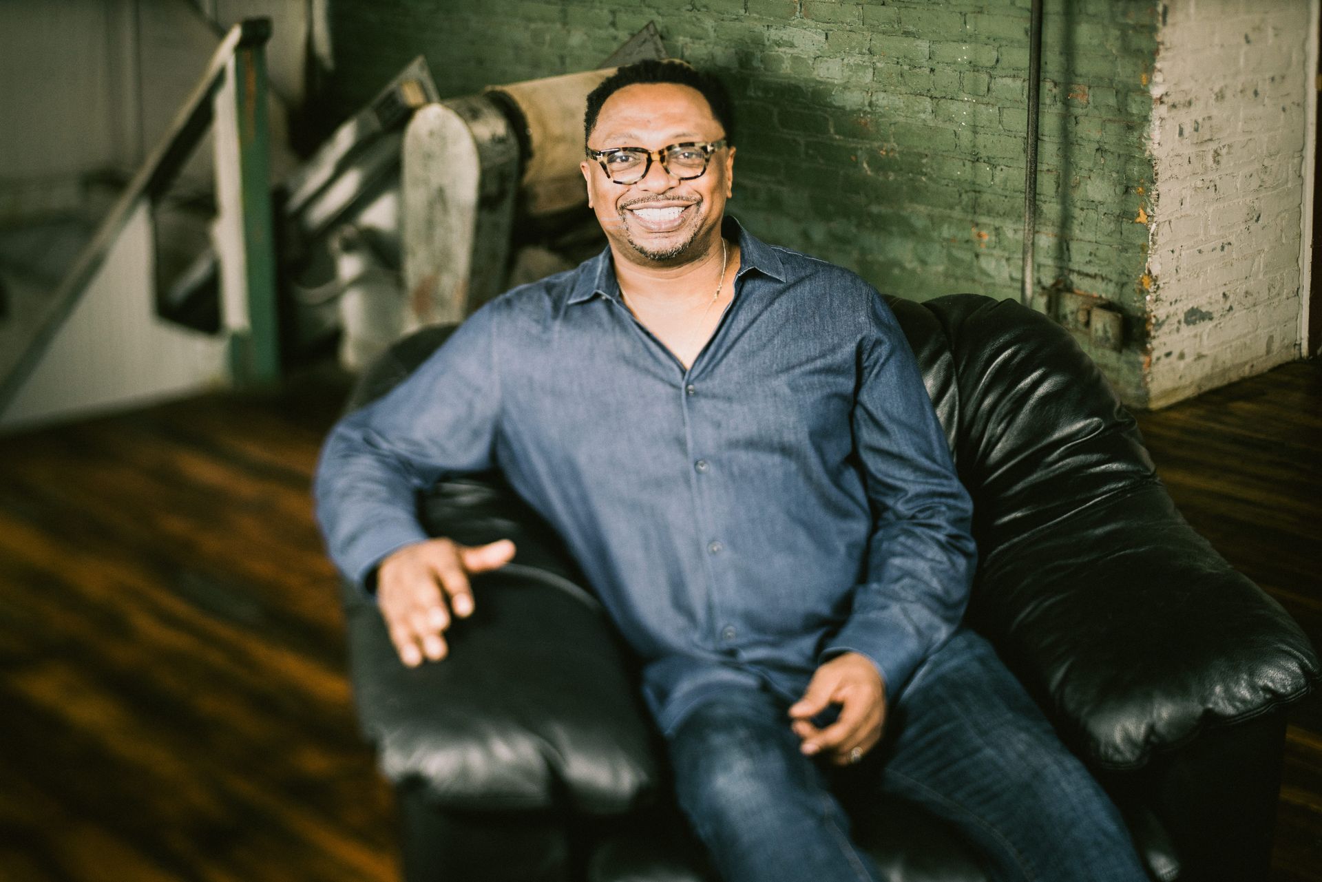 A man is sitting in a black leather chair and smiling.