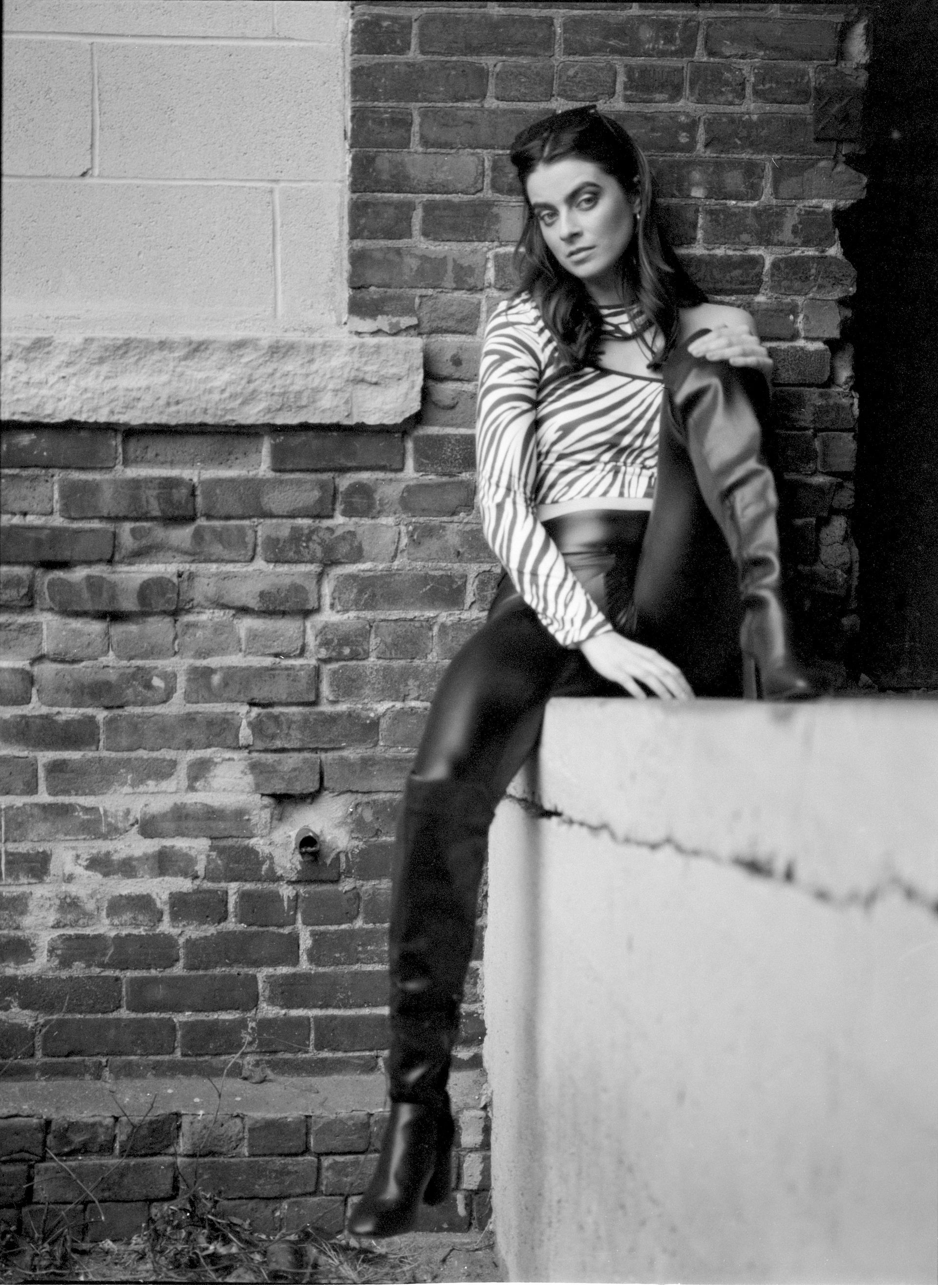 A woman is sitting on a concrete block in front of a brick wall.