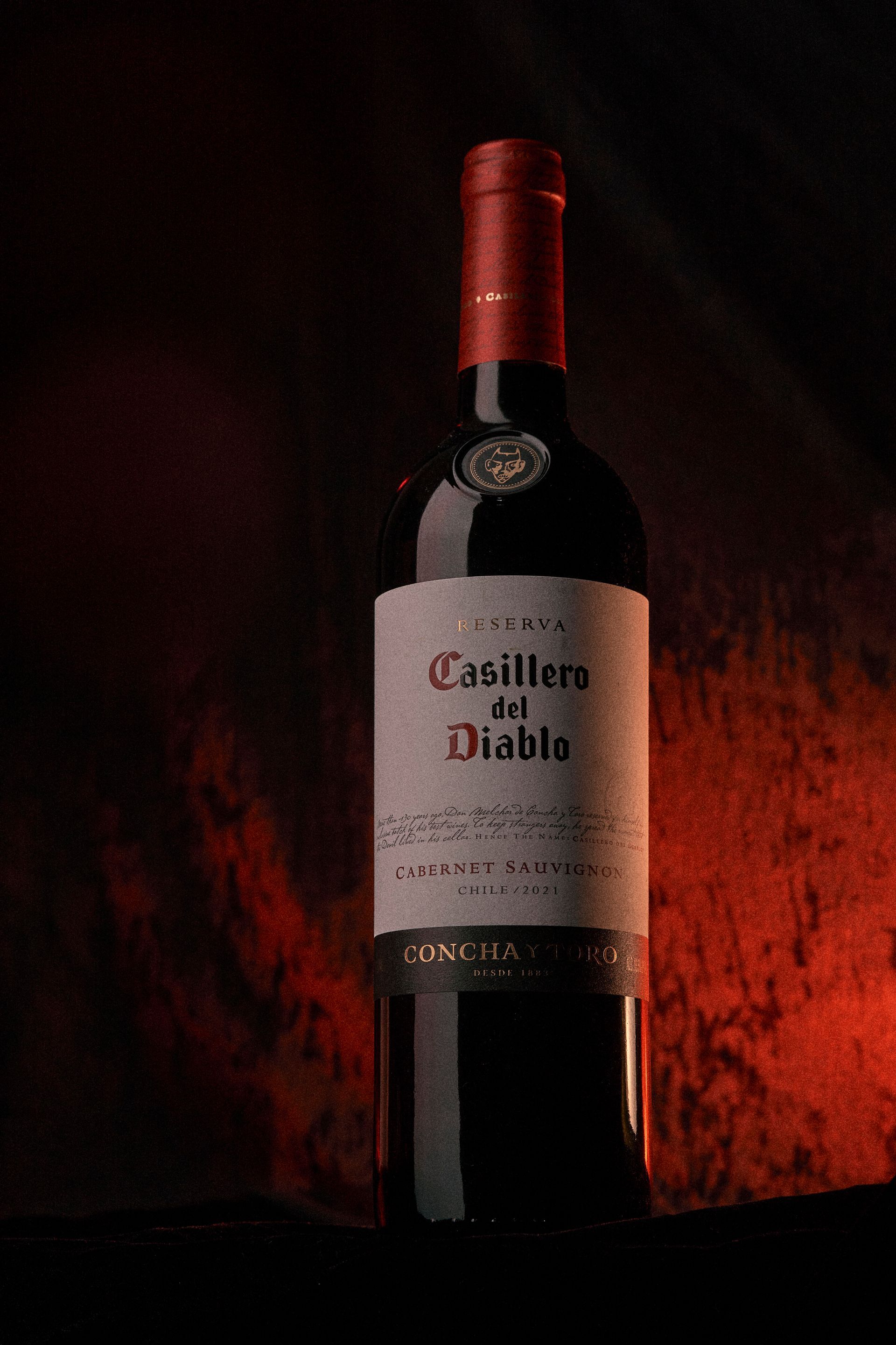 Bottle of Casillero del Diablo wine with red label against a dark red backdrop.