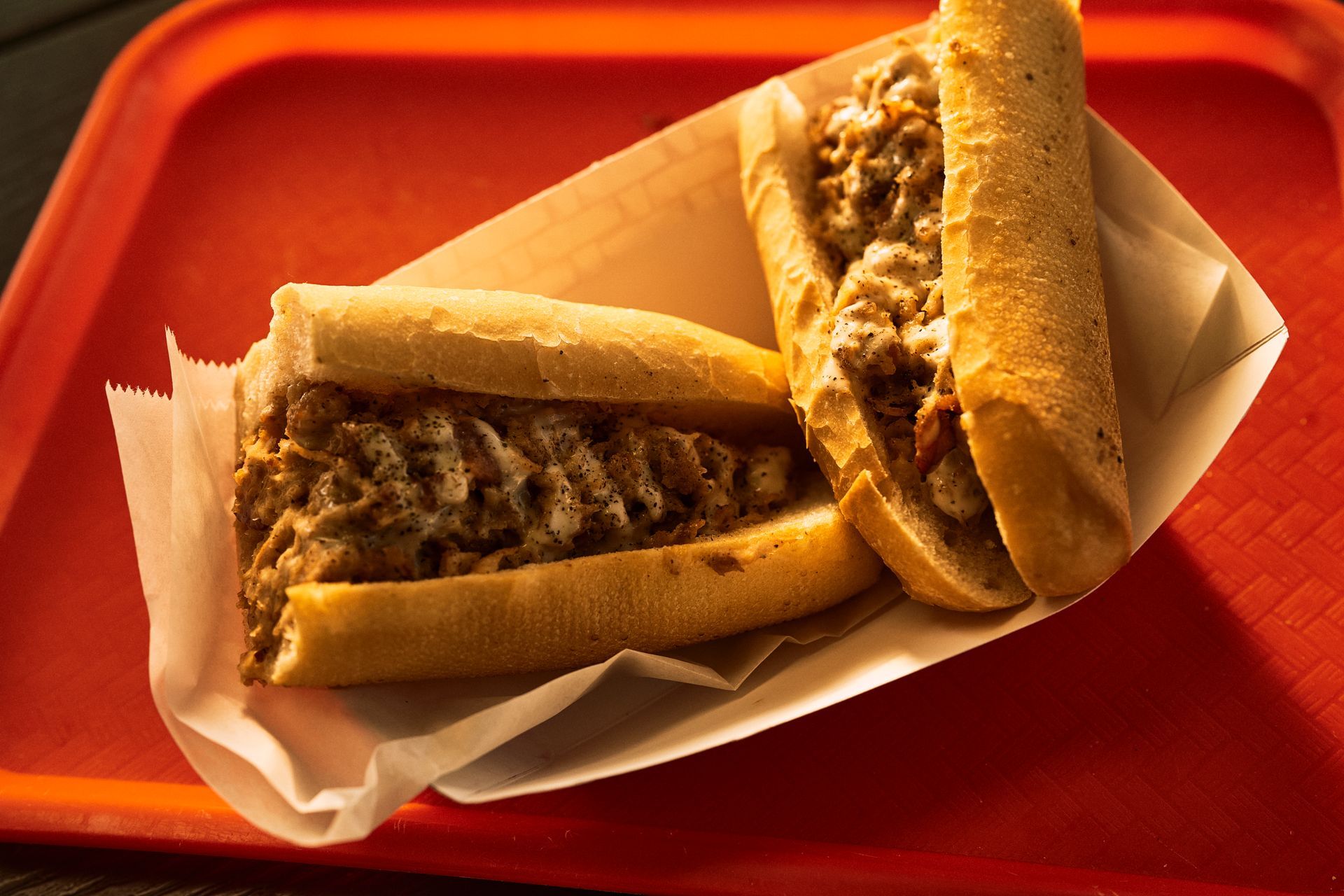 Two Philly cheesesteak sandwiches in paper on a red tray.
