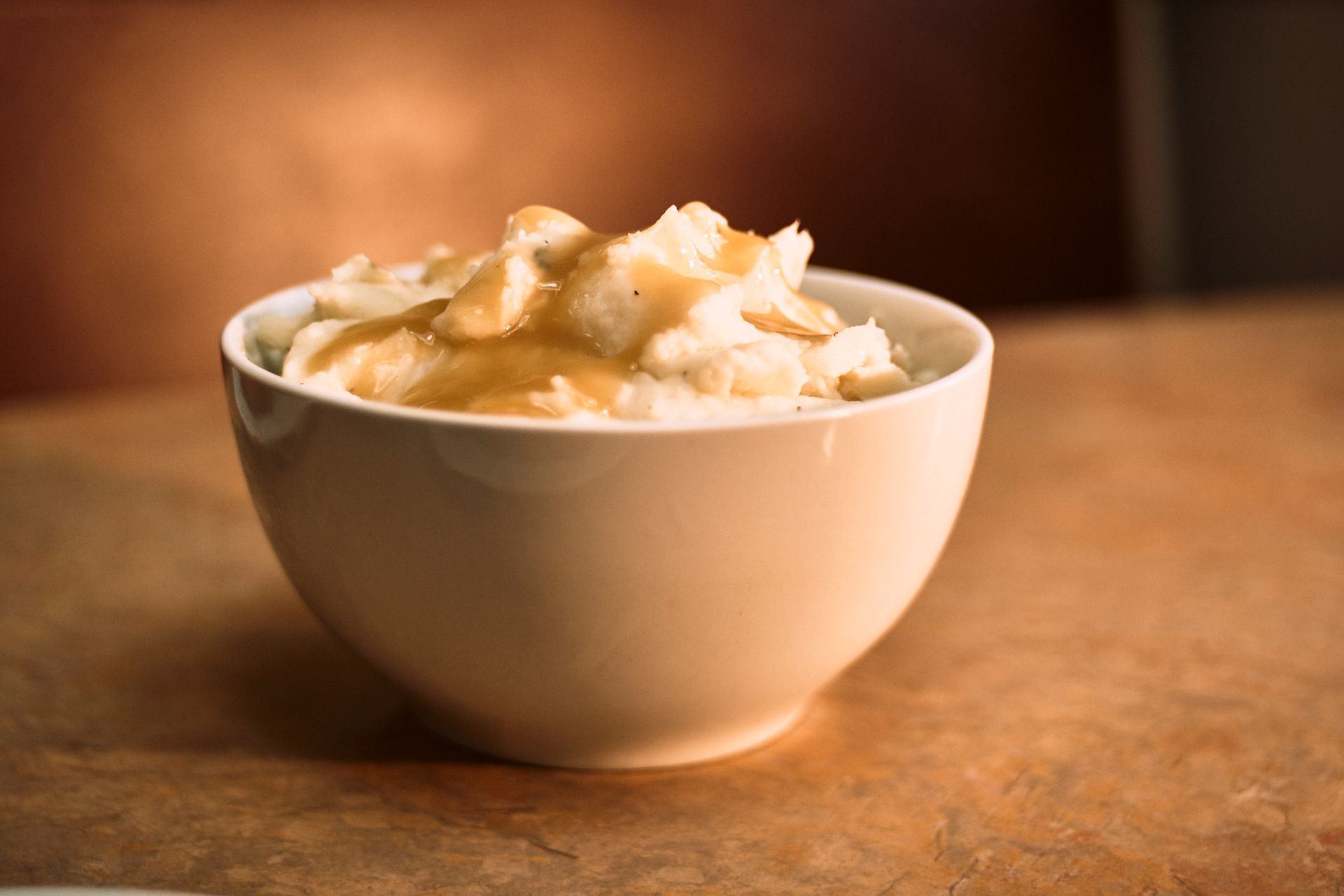 Bowl of mashed potatoes with gravy on a wooden surface.