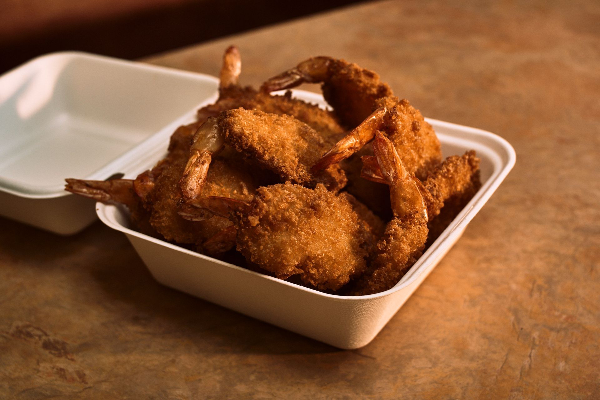 A styrofoam container filled with fried shrimp on a table.