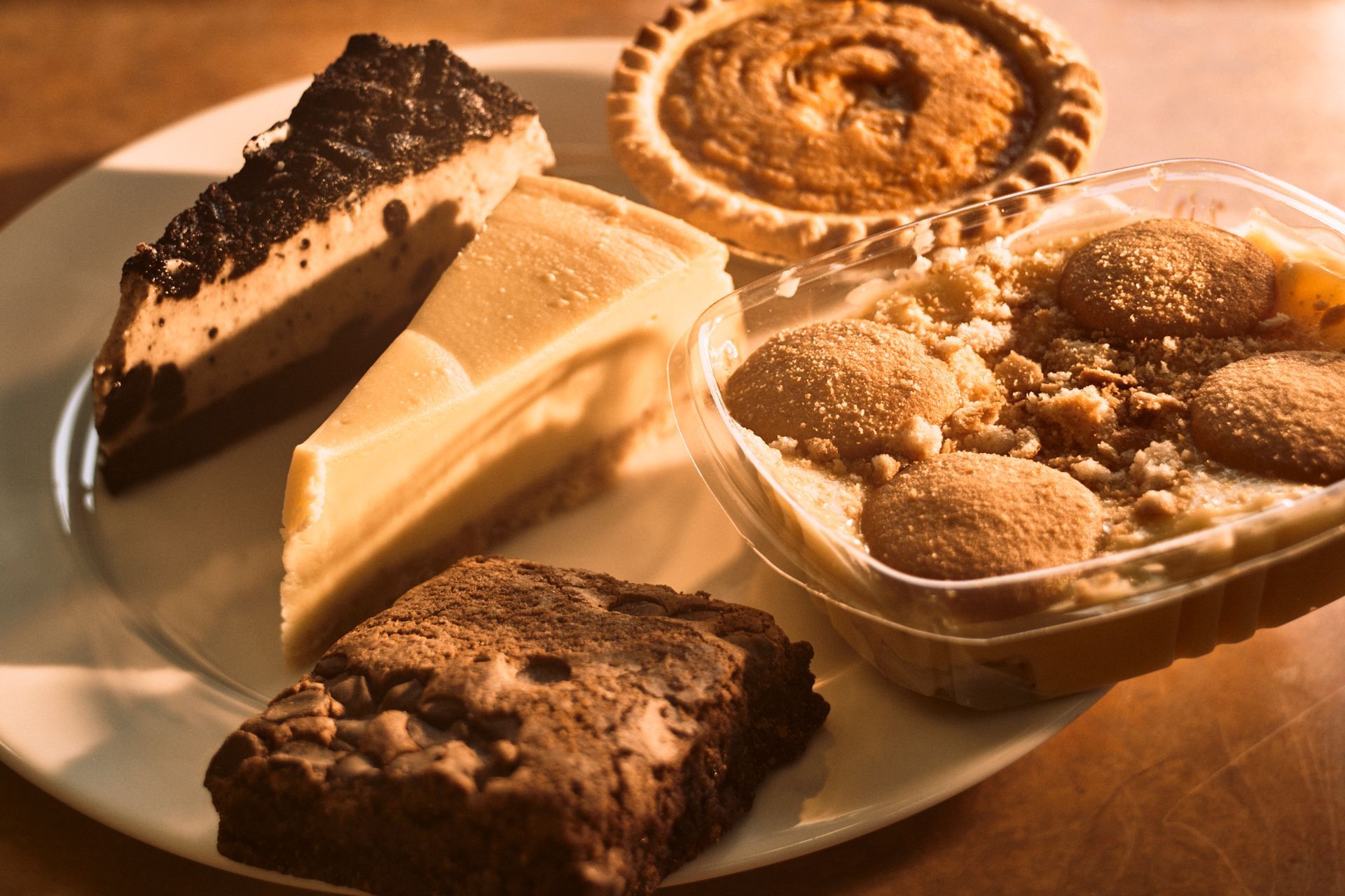Plate with various desserts: cheesecake, brownie, pie, and banana pudding.