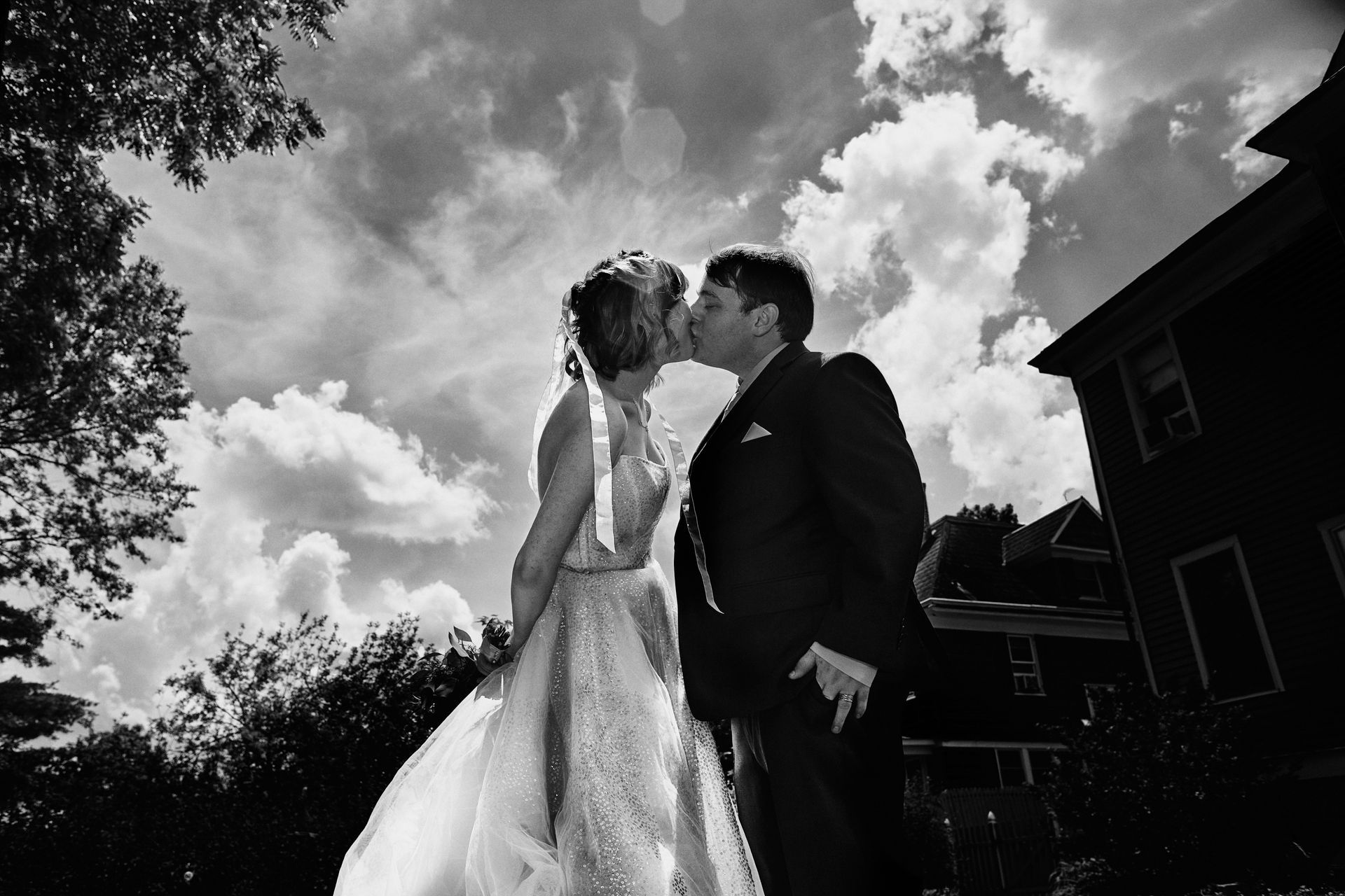 A bride and groom are kissing in front of a building in a black and white photo.