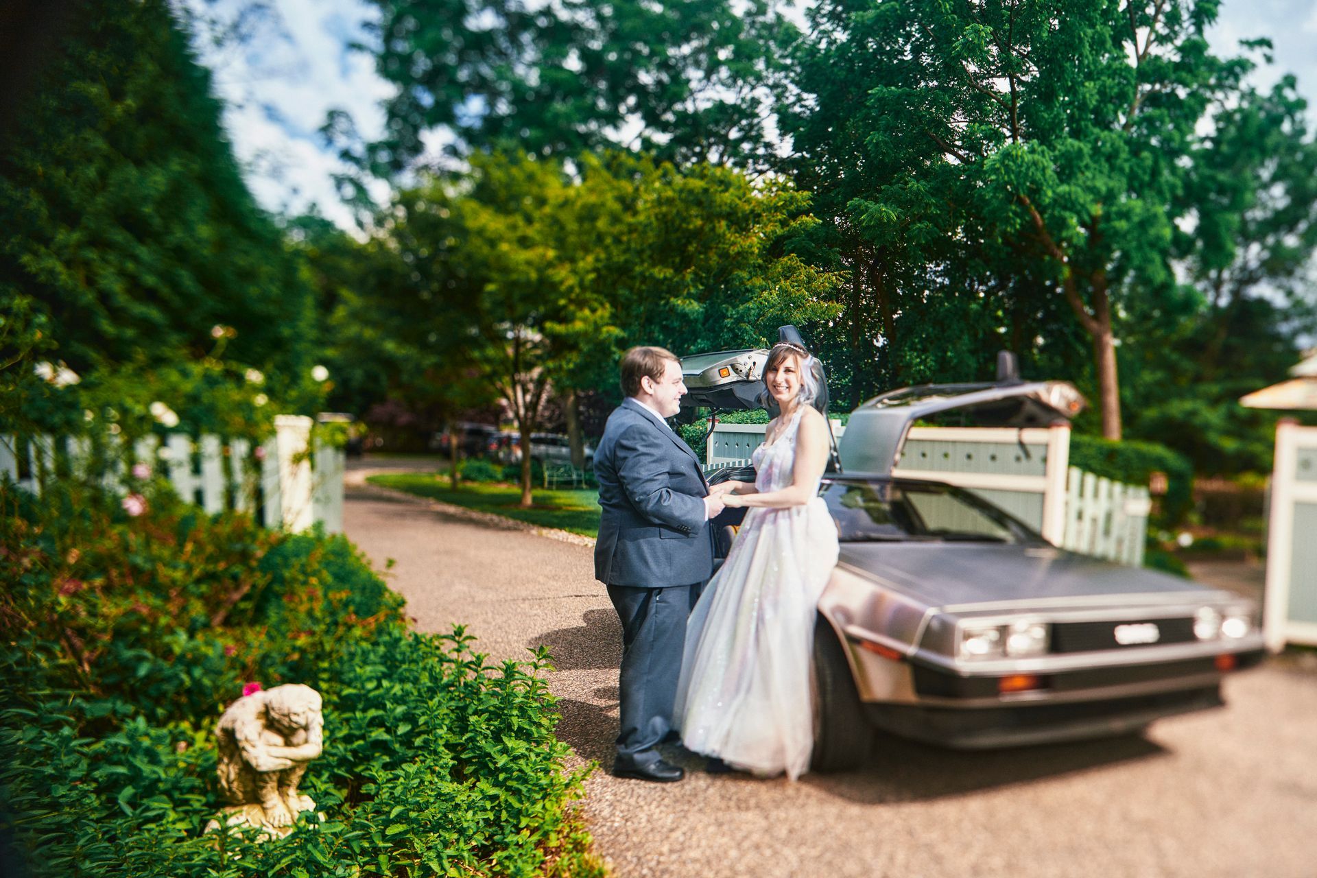 A bride and groom are standing next to a back to the future car.