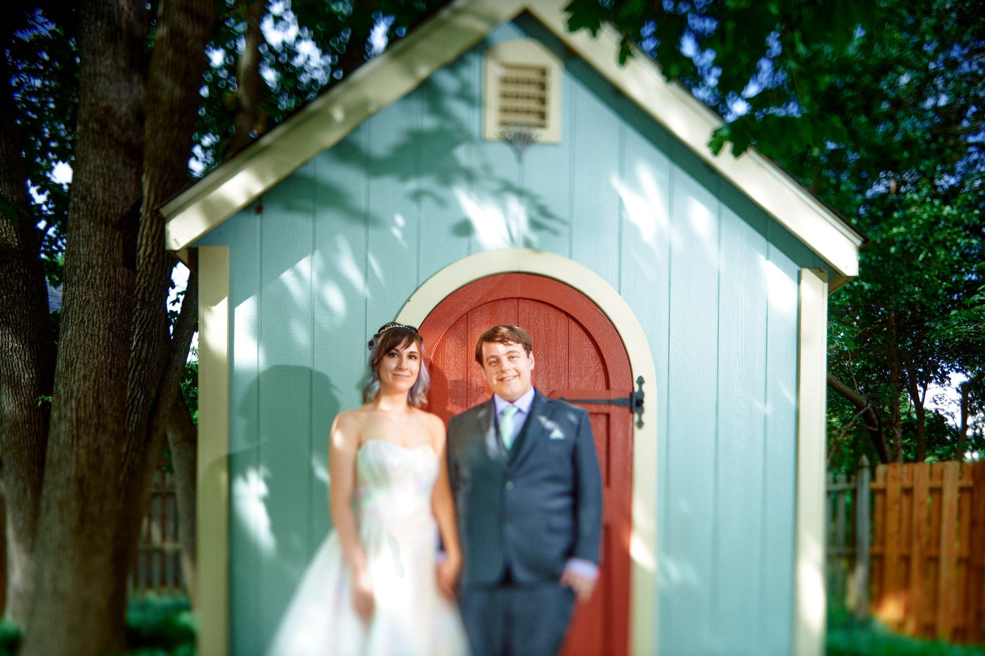 A bride and groom pose in front of a blue shed