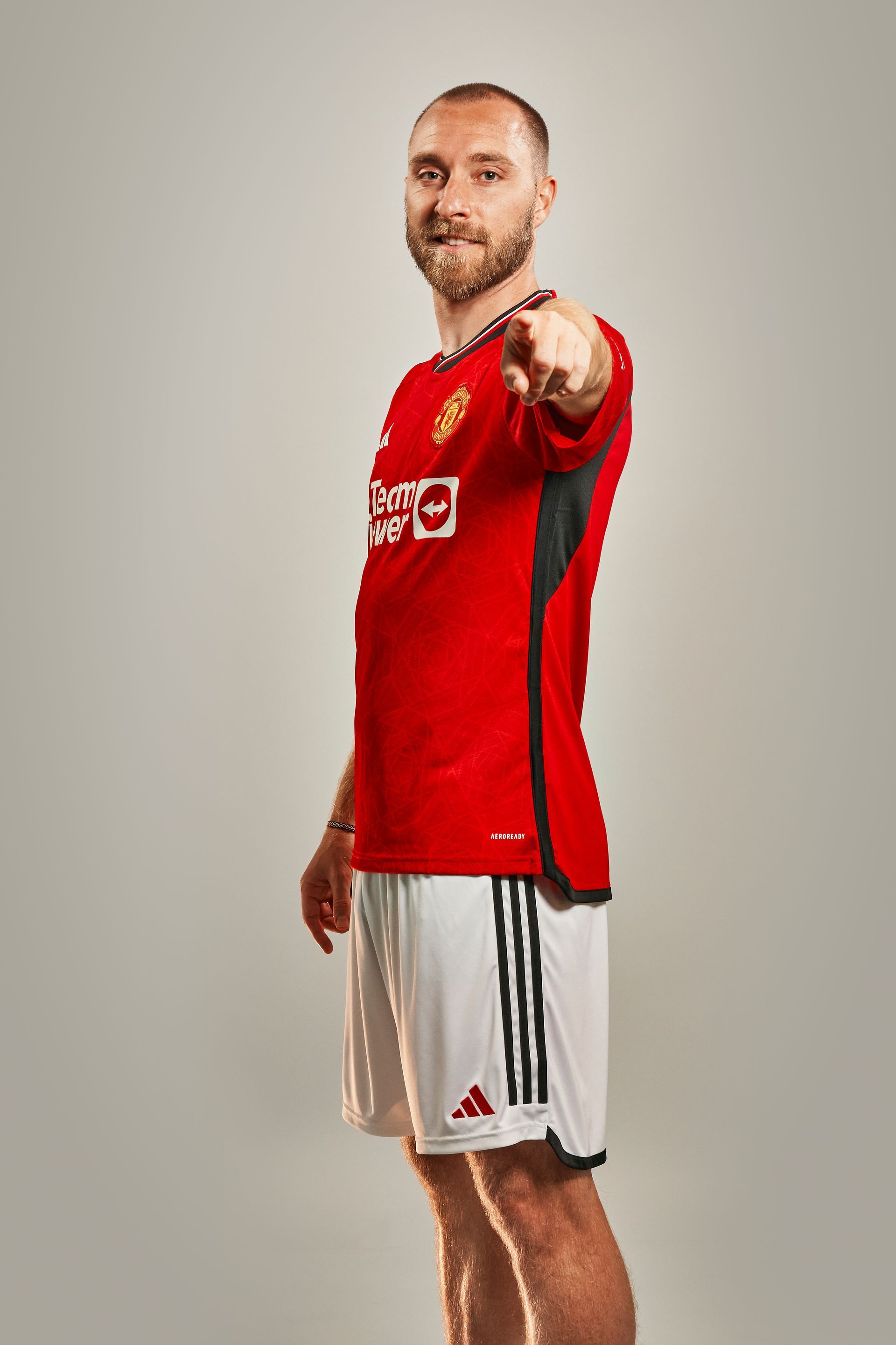 A man in a red shirt and white shorts is pointing at the camera.