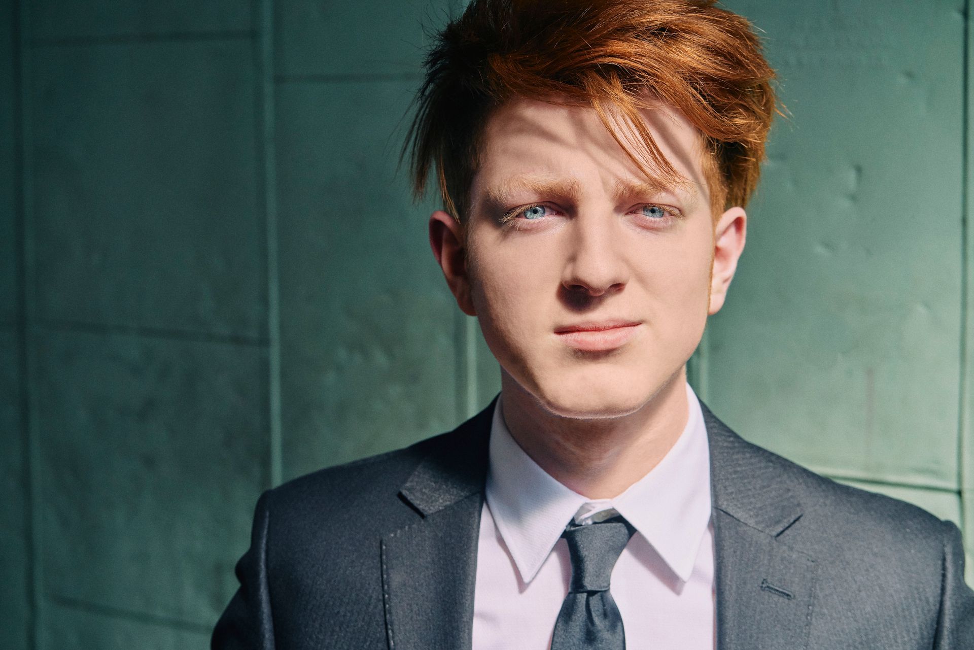 A young man with red hair is wearing a suit and tie.