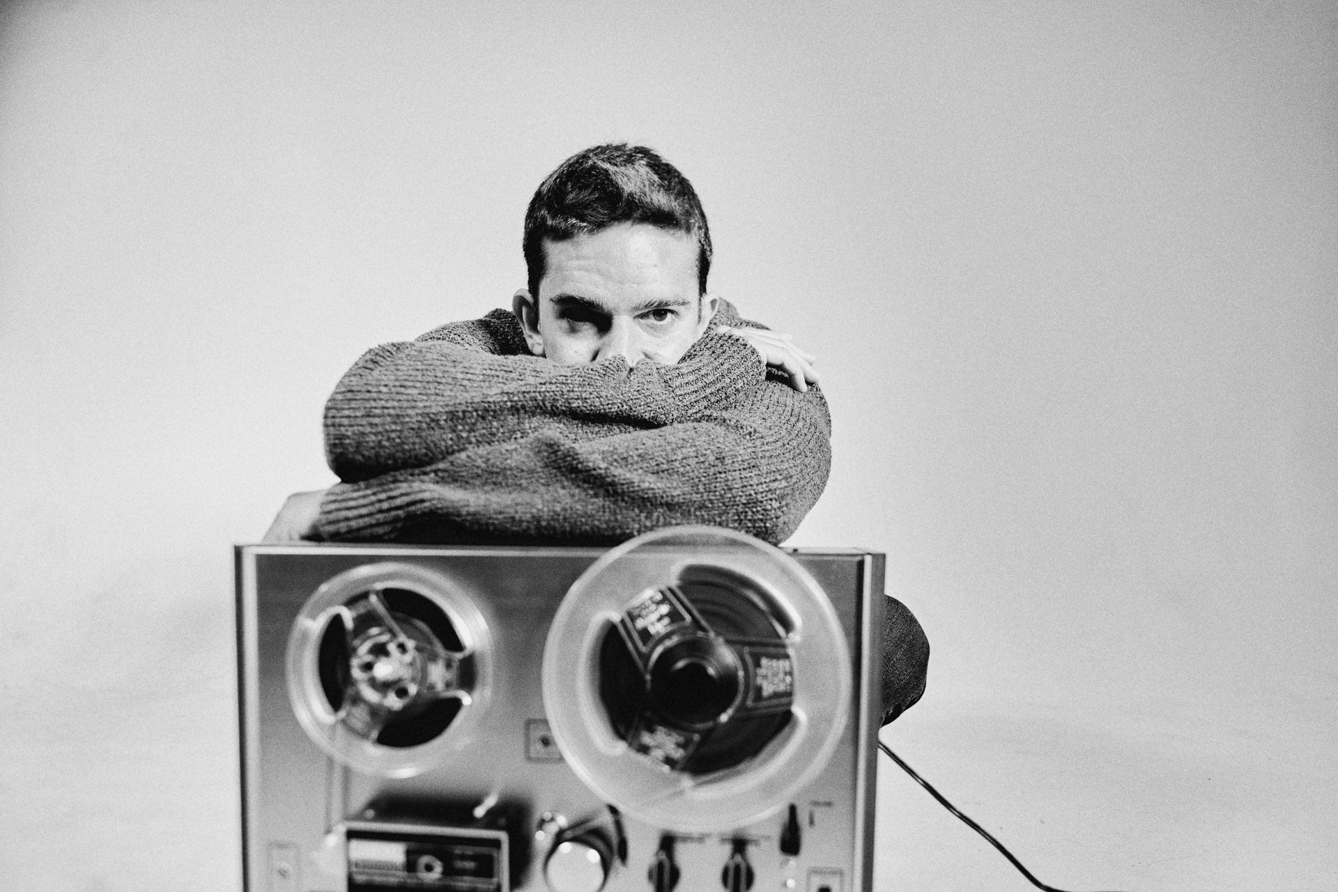 A black and white photo of a man sitting on a tape recorder