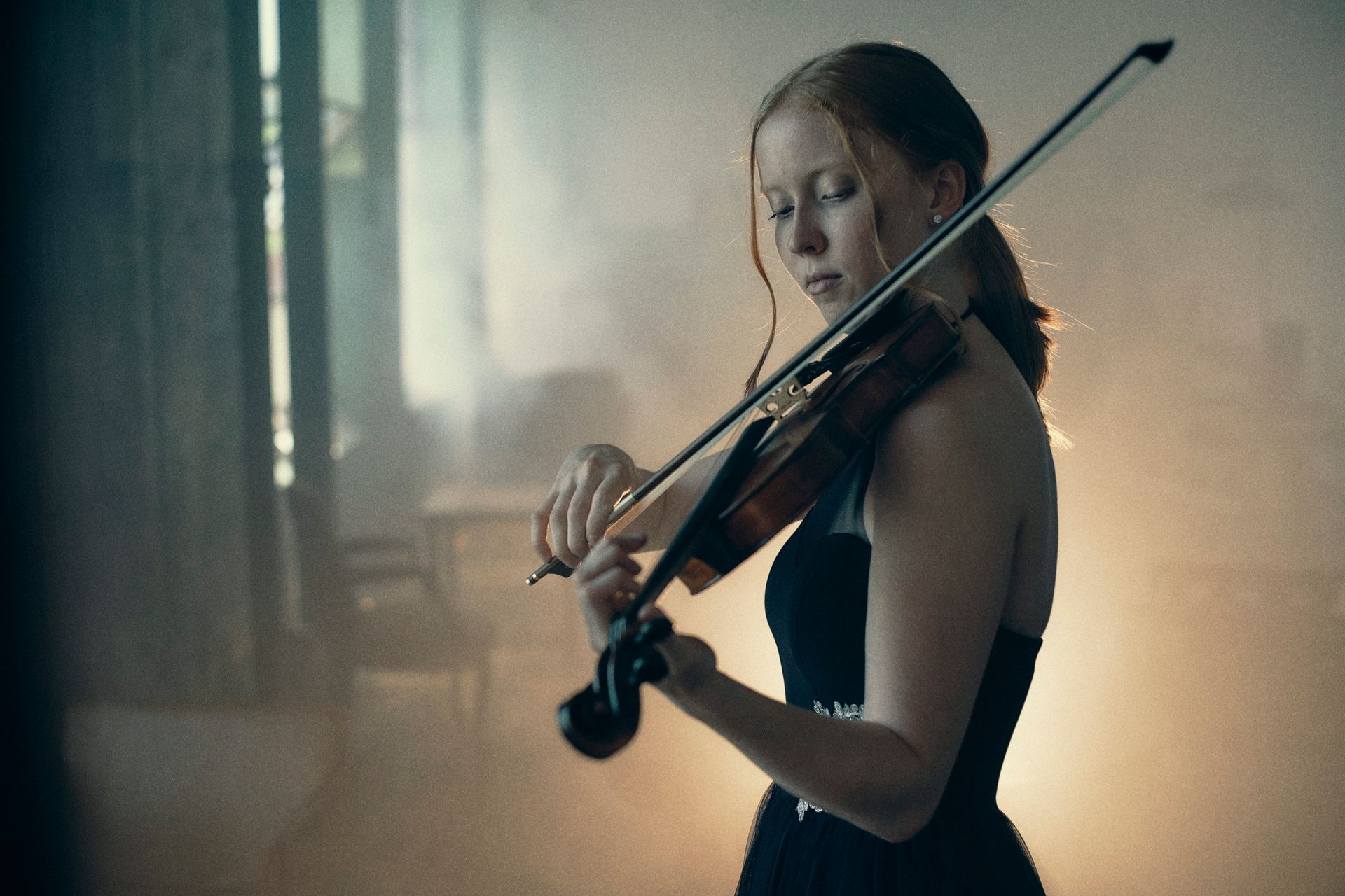 A woman in a black dress is playing a violin.