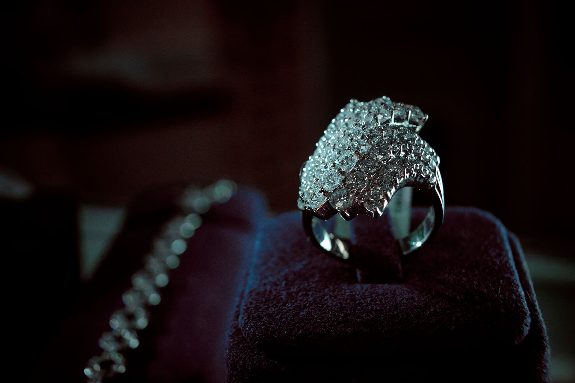 Diamond-encrusted ring sits on a velvet stand, with a silver chain in the background.