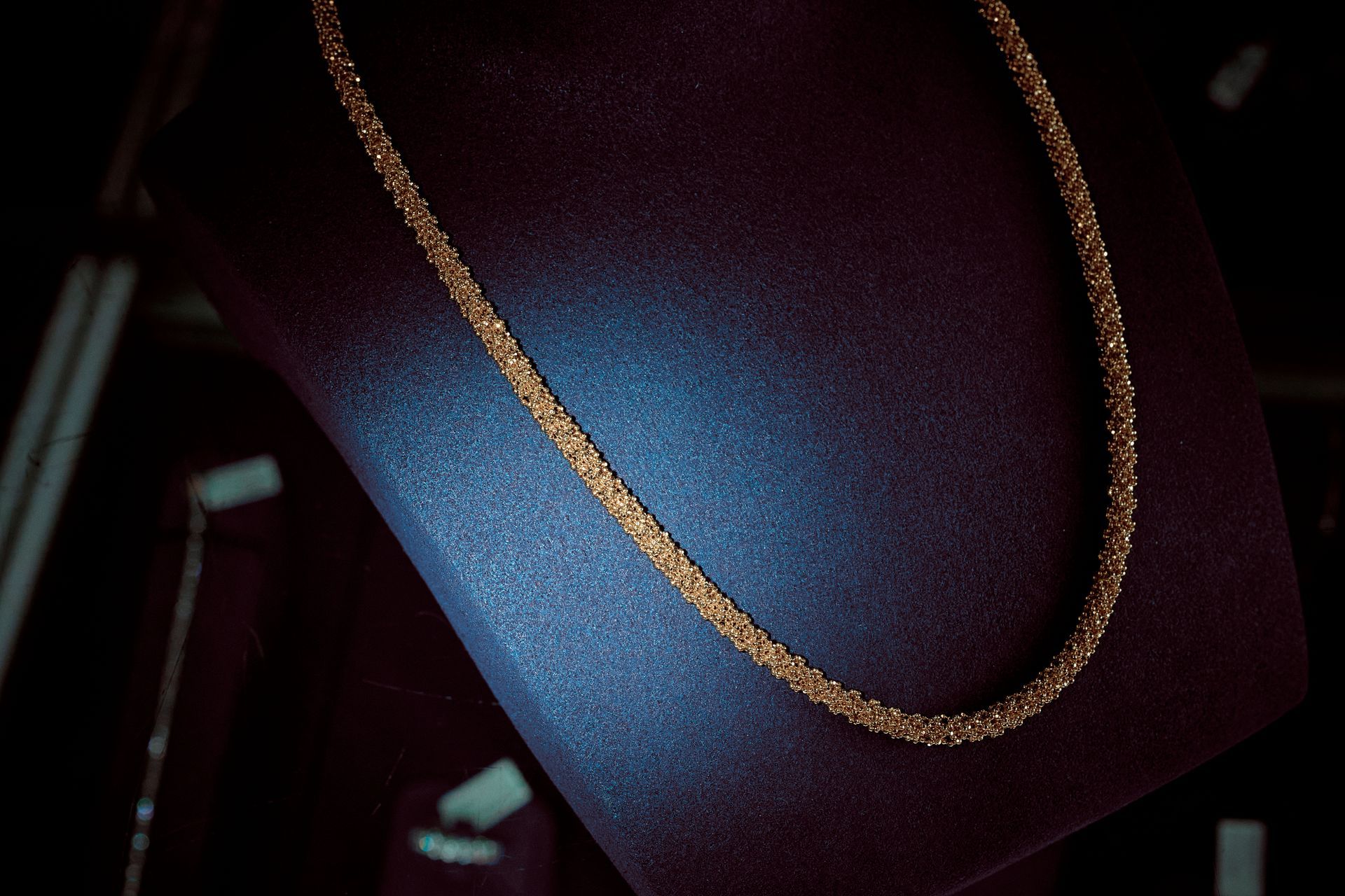 Gold necklace displayed on a dark blue velvet jewelry stand.