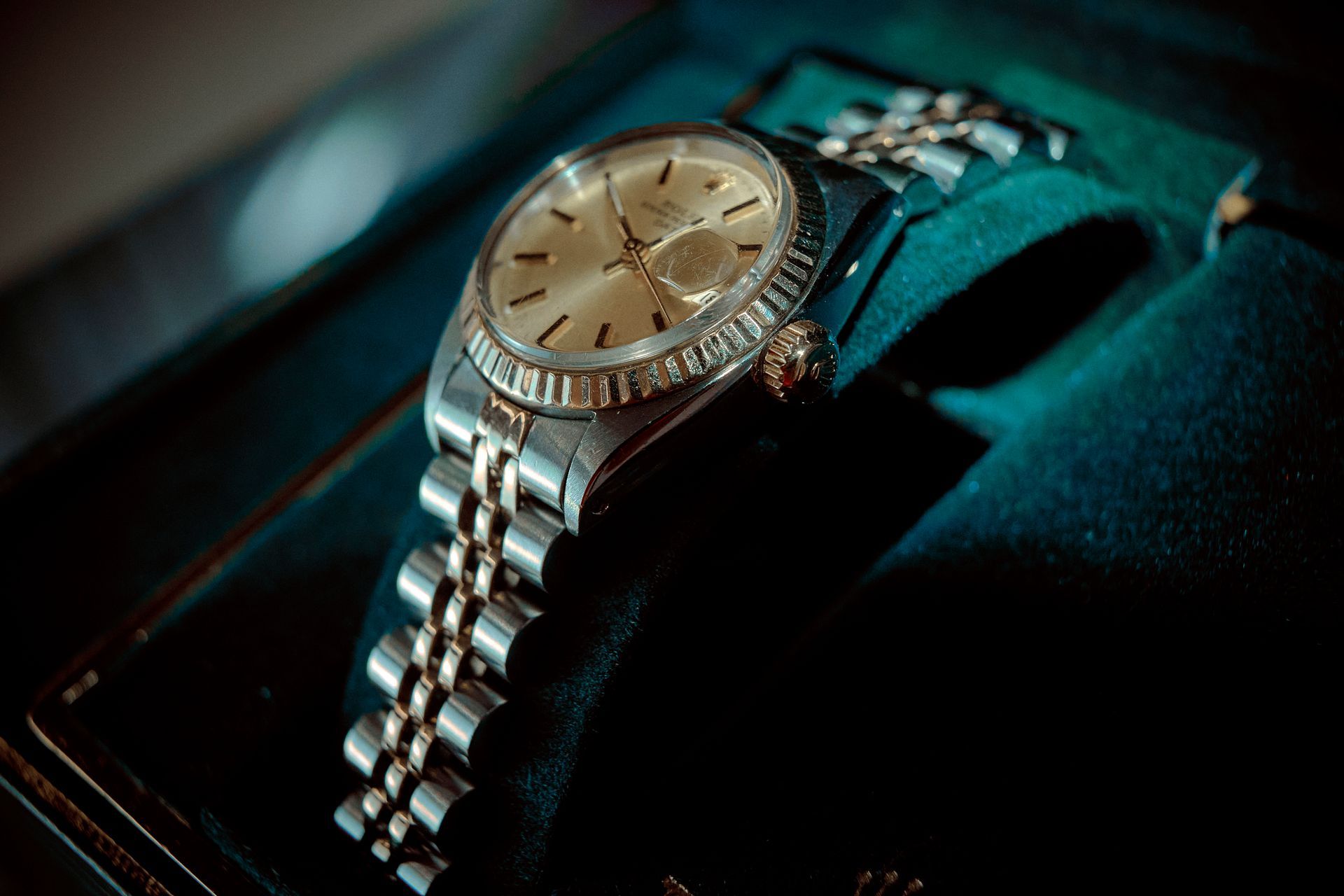 Silver Rolex watch with gold face on a velvet green display.