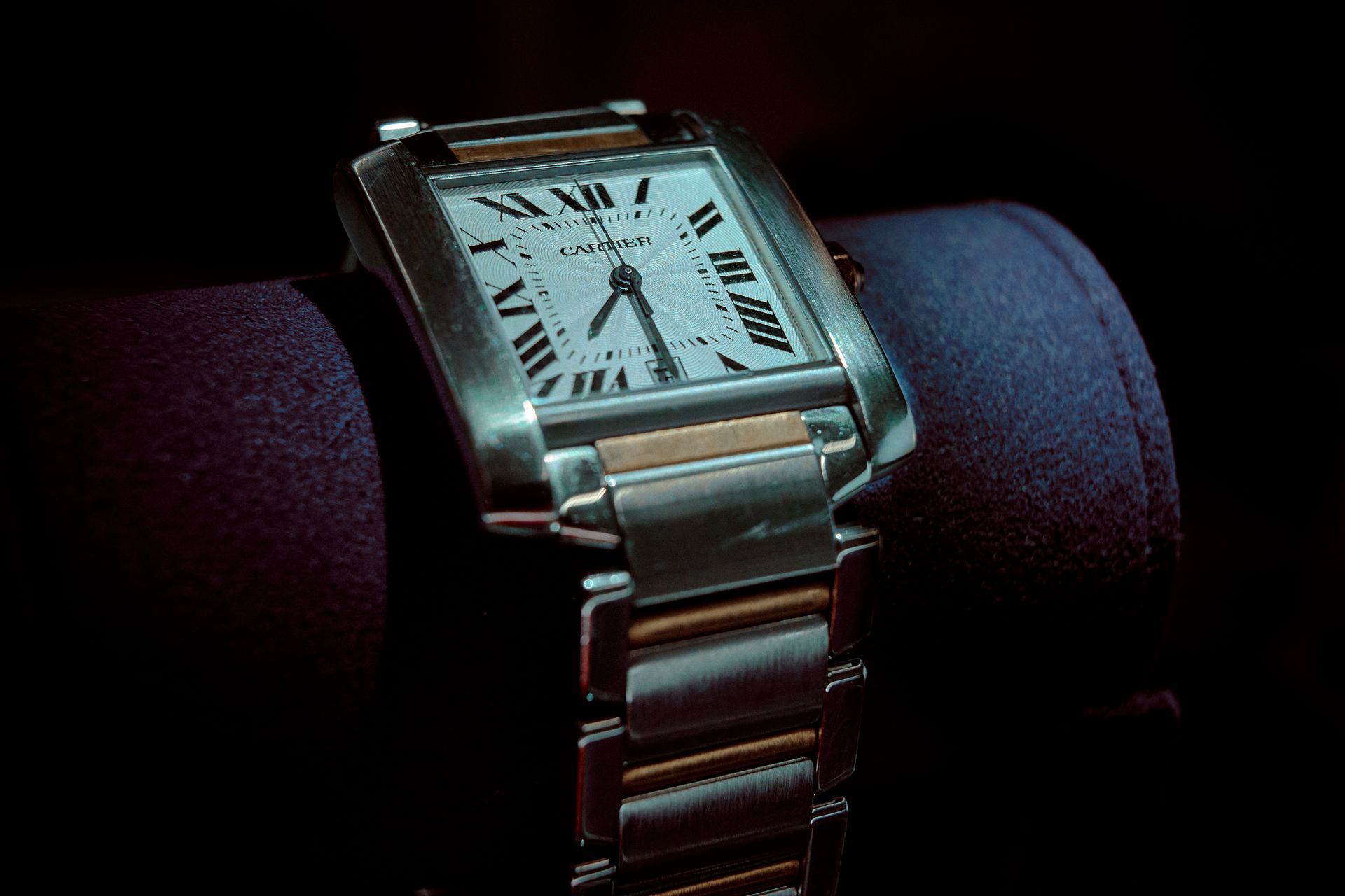 Cartier watch with silver and gold accents on a dark purple surface, black background.