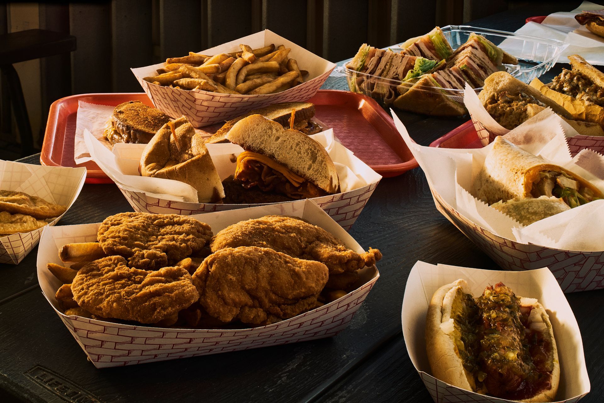 Assortment of fast food items: fried chicken, sandwiches, fries, and tacos in paper baskets on a table.
