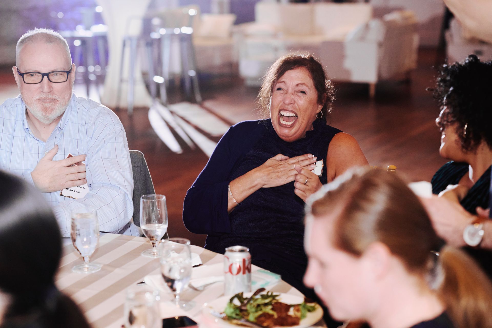 People laughing together at a dinner table in a bright restaurant, mid-conversation and enjoying a meal.