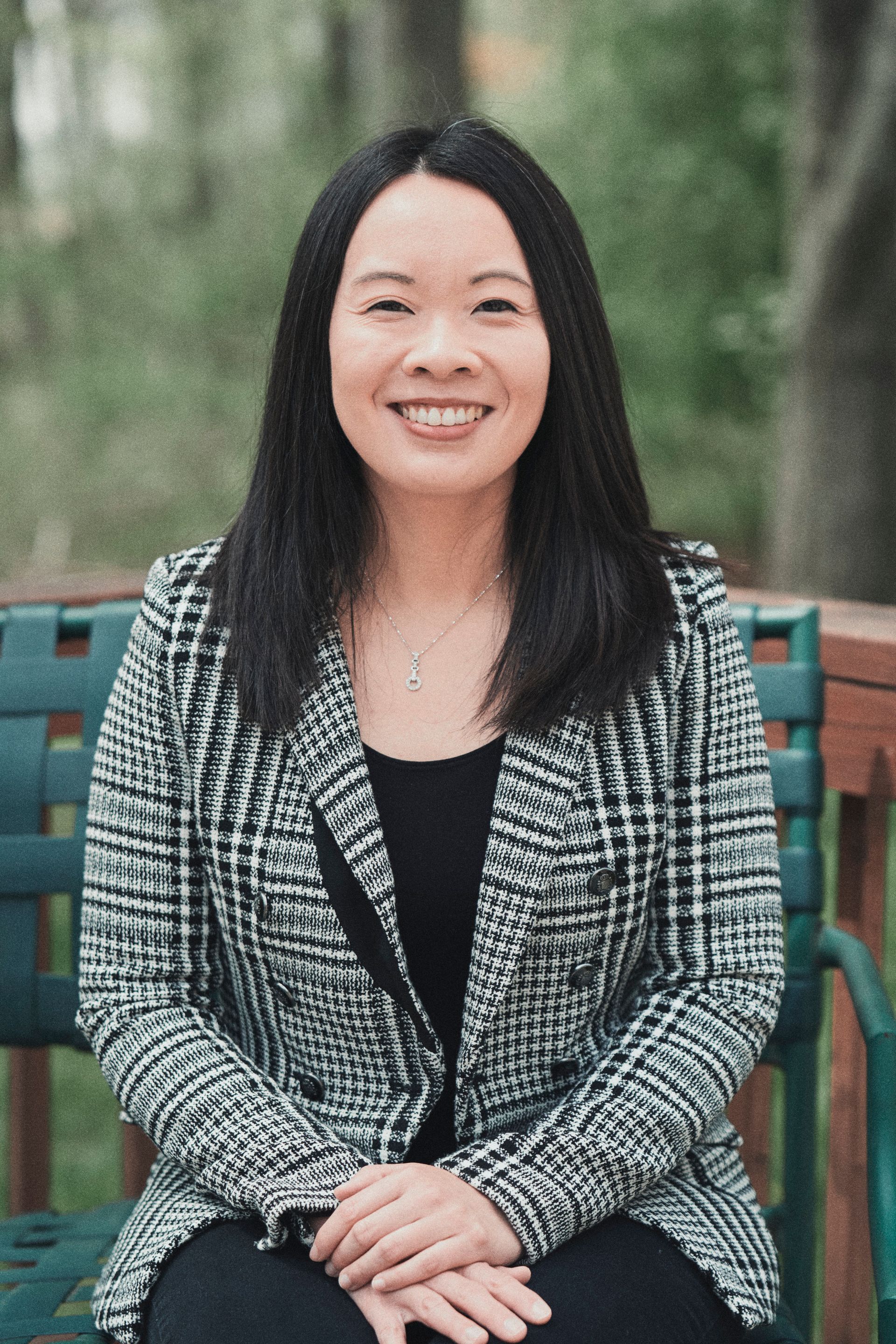 A woman is sitting on a chair with her hands folded and smiling.