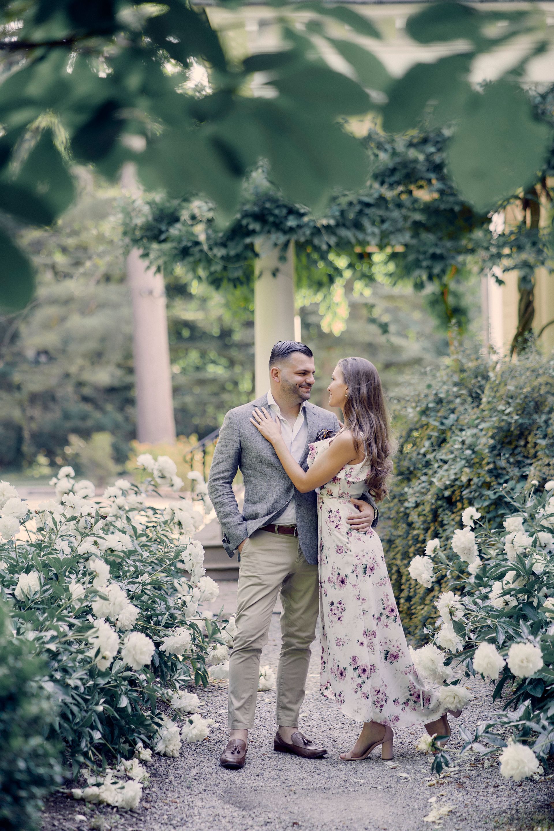 A man and a woman are standing next to each other in a garden surrounded by white flowers.