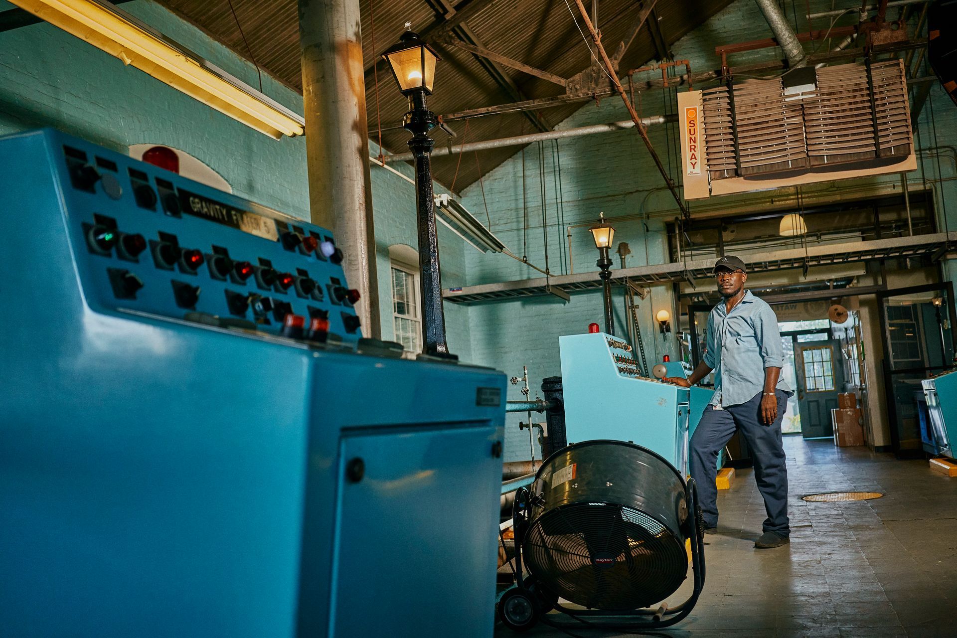 A man is standing in a room with a fan and a control panel.