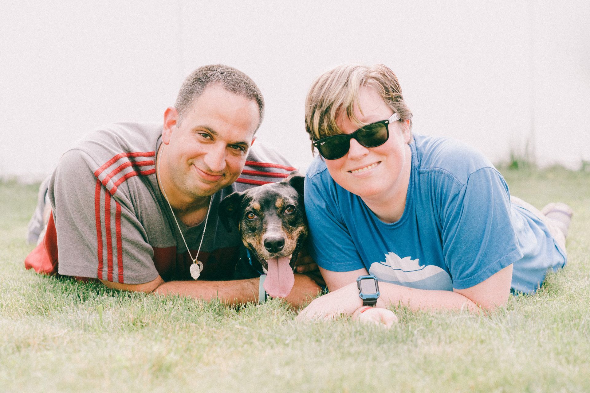 A man and woman are laying in the grass with their dog.