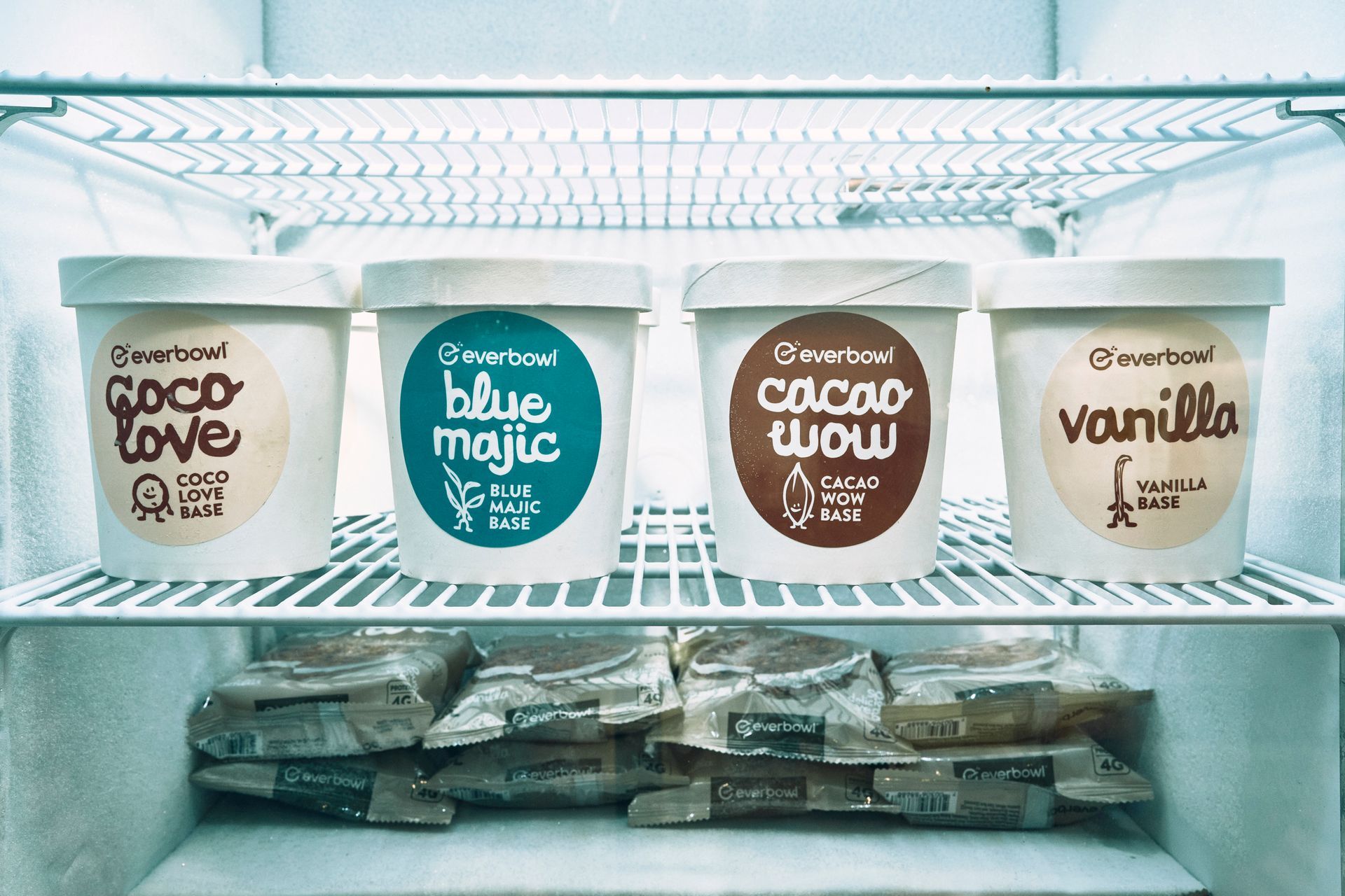 Ice cream tubs in a freezer: Coco Love, Blue Majic, Cacao Wow, and vanilla. Bags of frozen product below.