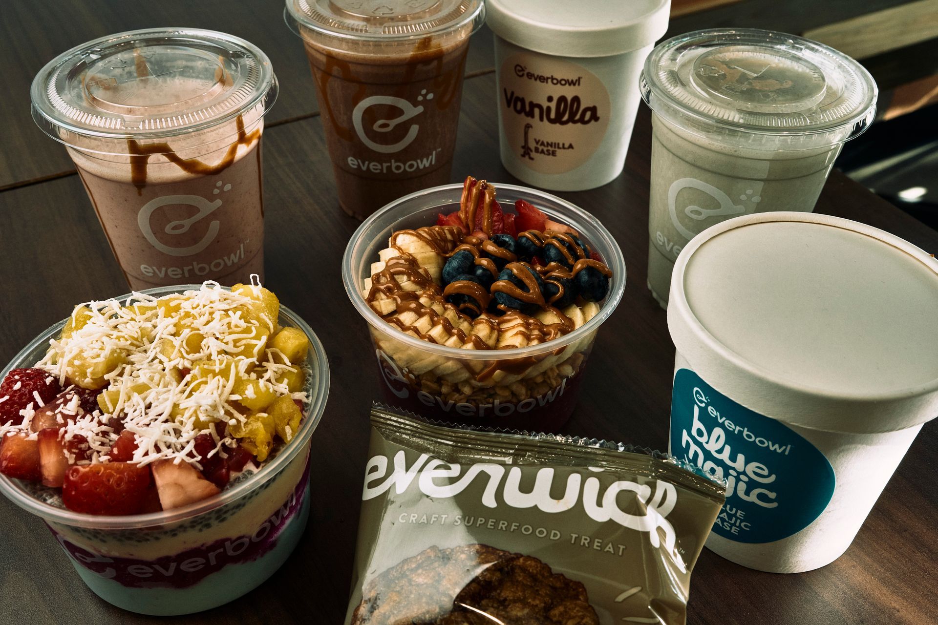 Bowls and drinks from Everbowl: fruit, acai, chocolate smoothies, snack bar on a wood table.