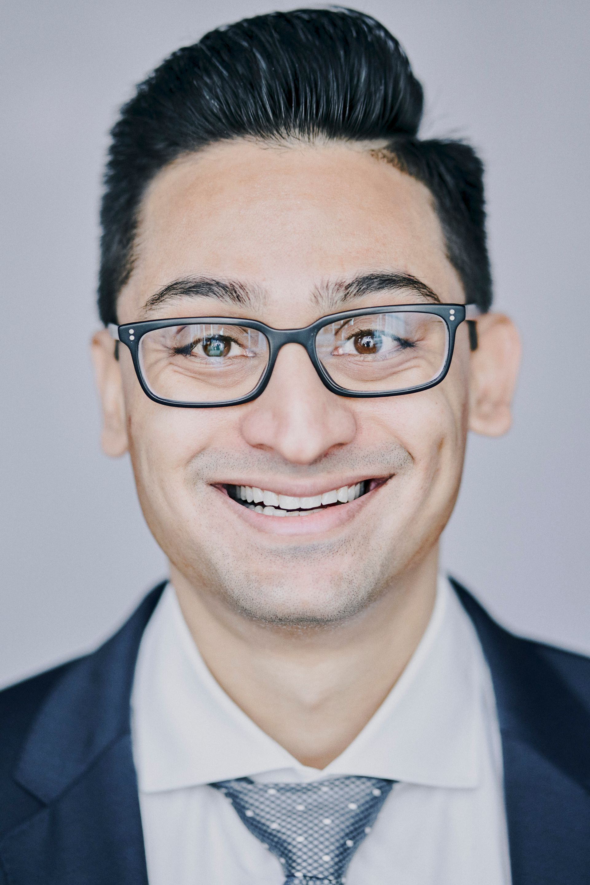 A man wearing glasses and a tie is smiling for the camera.