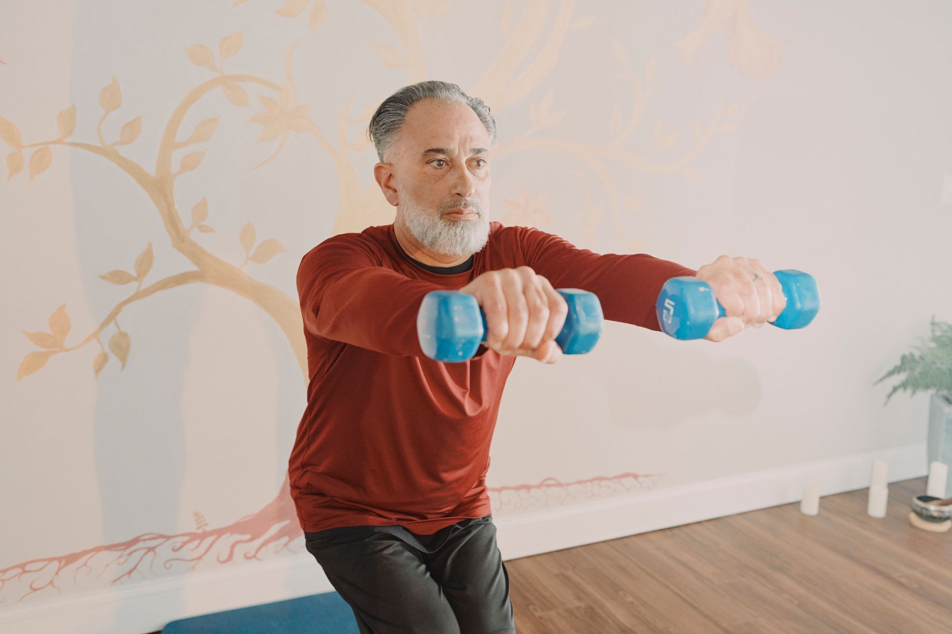Man doing seated arm raises with blue dumbbells in a bright room