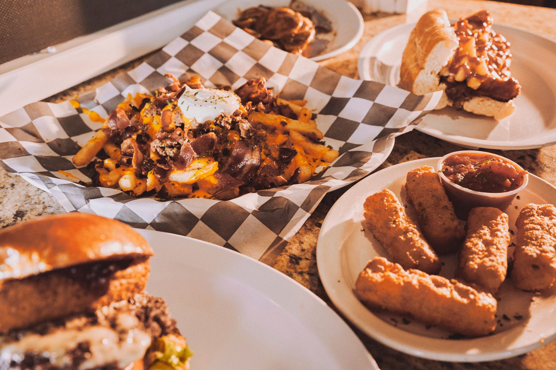 Various plates of American food: fries, burger, hot dog, and fried cheese sticks.