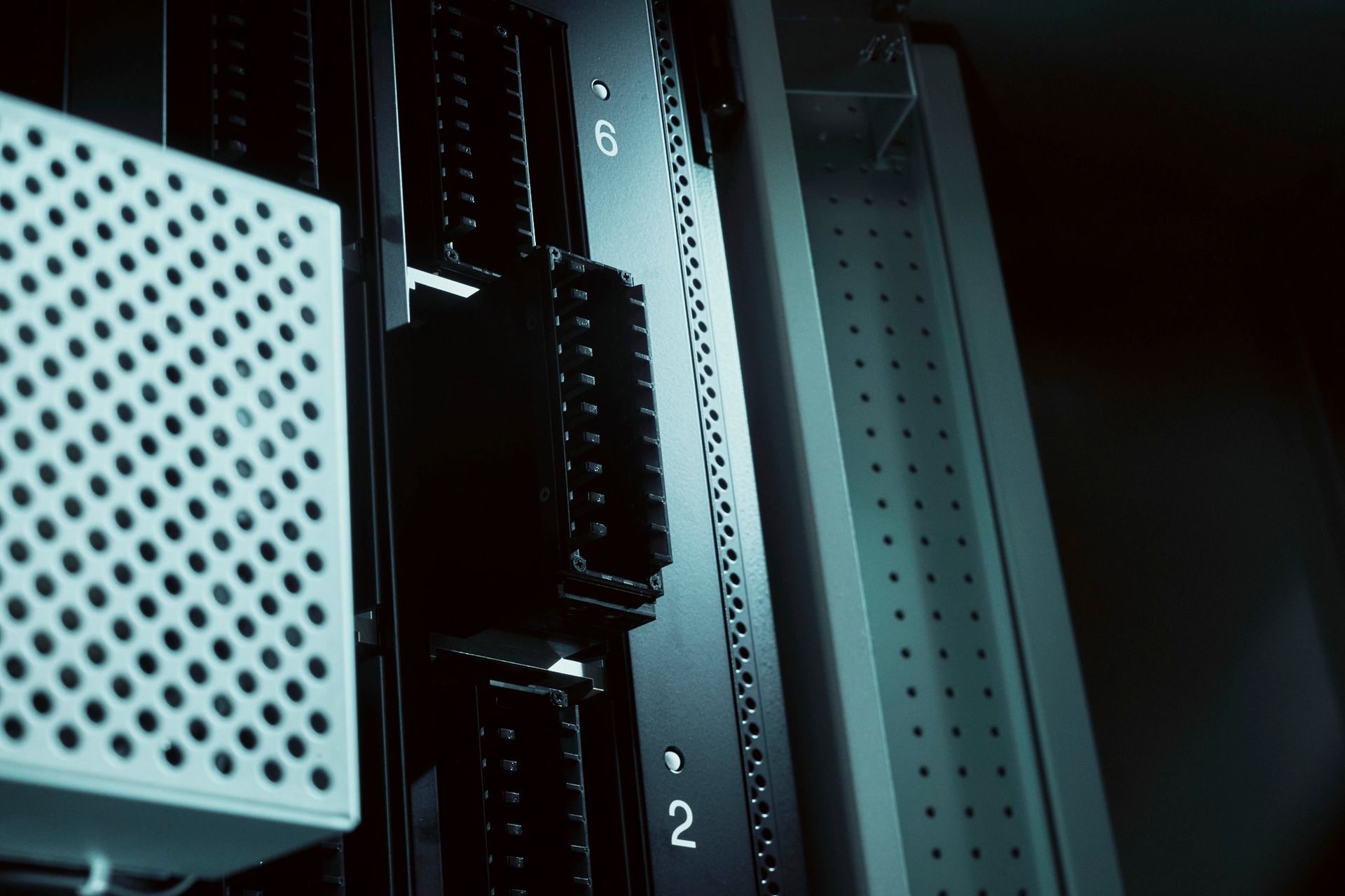 Server rack with equipment, close-up view. Dark tones with a perforated metal box on the left.