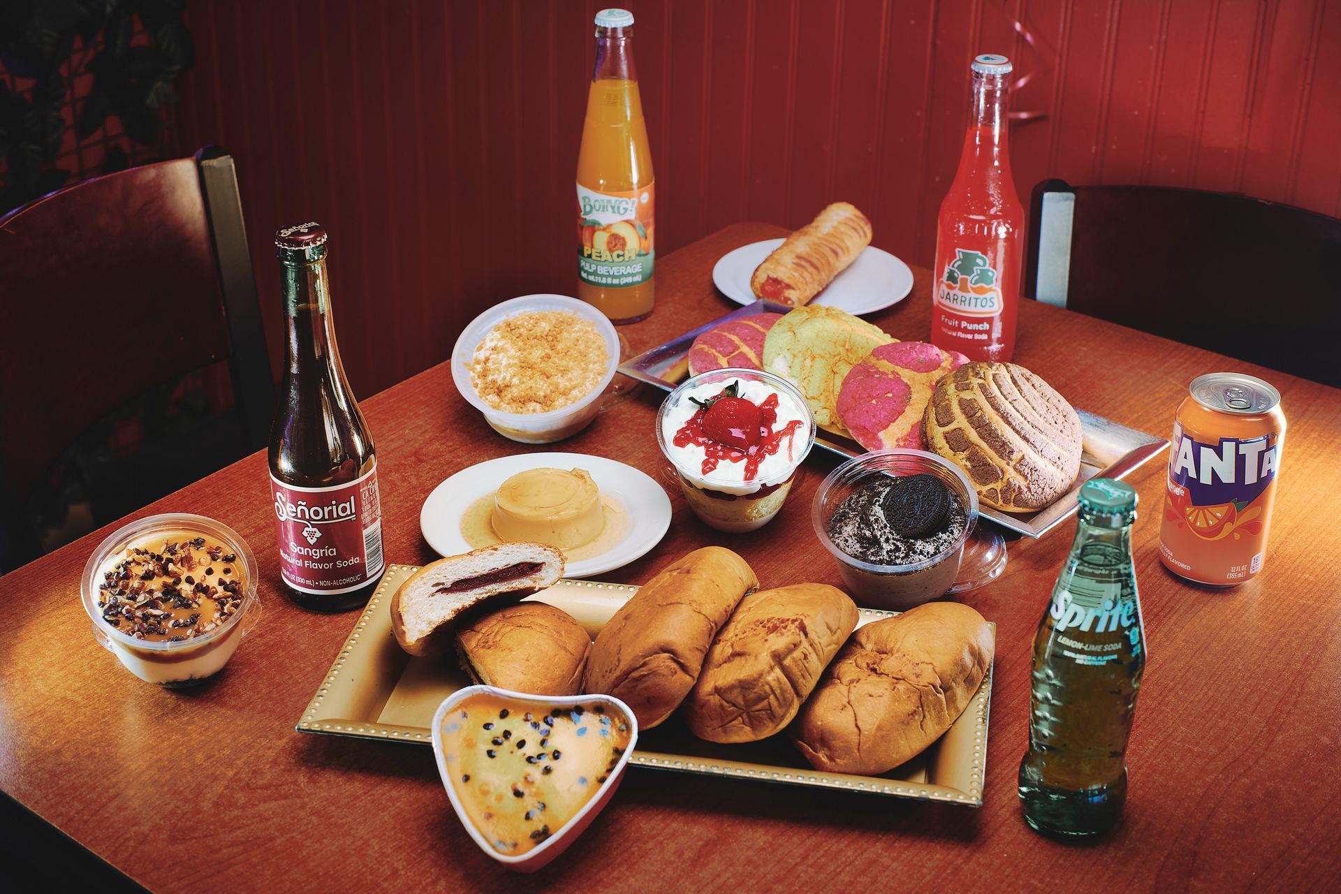 Table of various foods and drinks: pastries, cakes, juices, sodas, and a beer bottle.