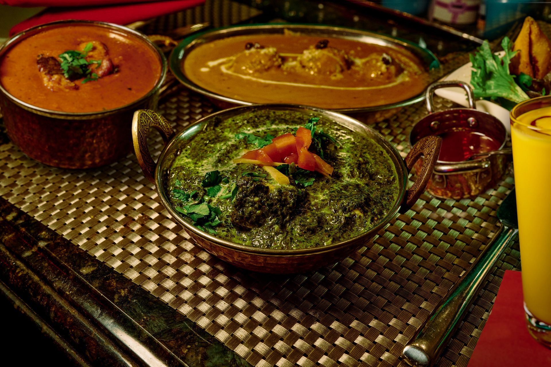 Indian cuisine: Three curry dishes, with orange drink, on a patterned surface.
