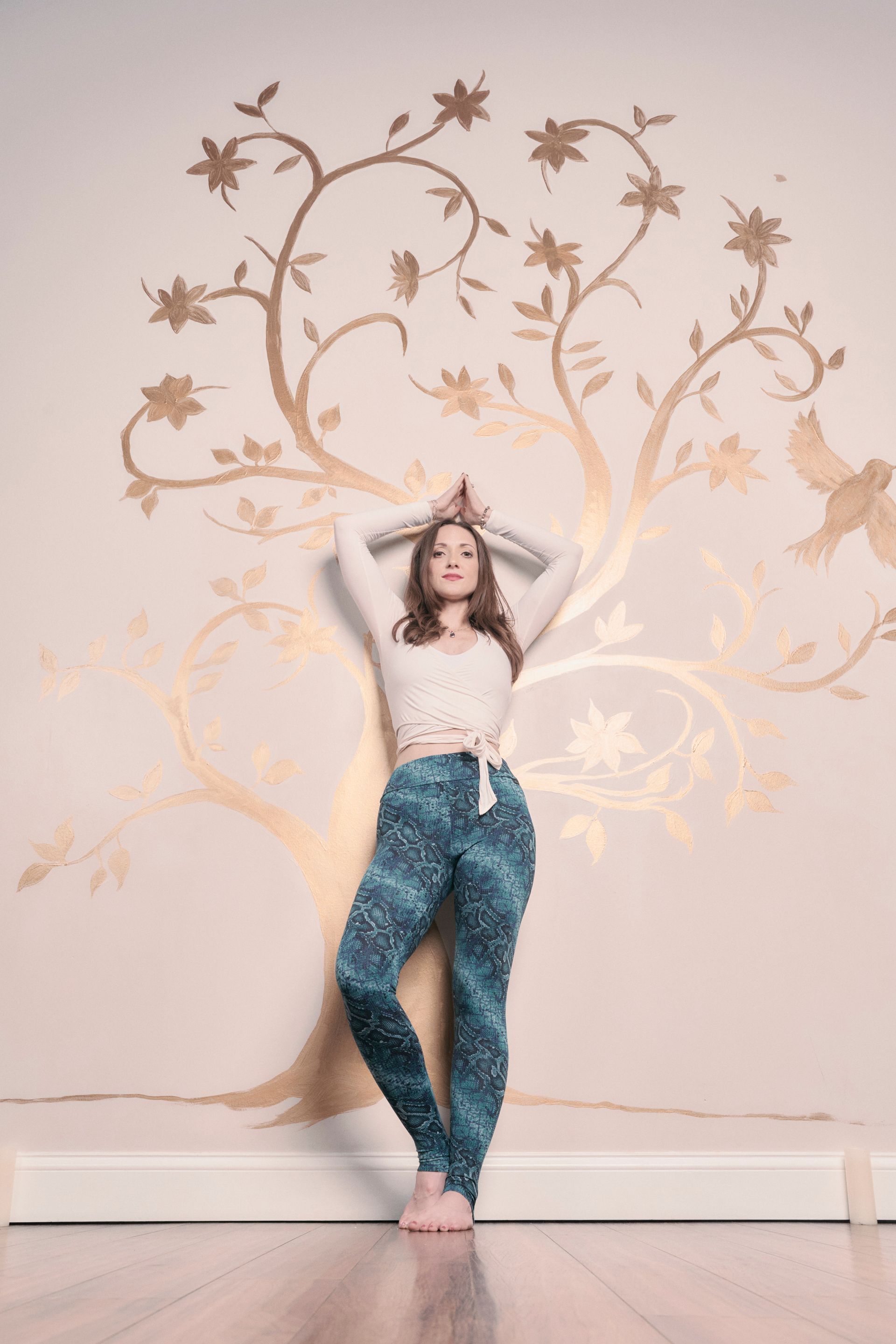 A woman is standing in front of a wall with a tree painted on it.