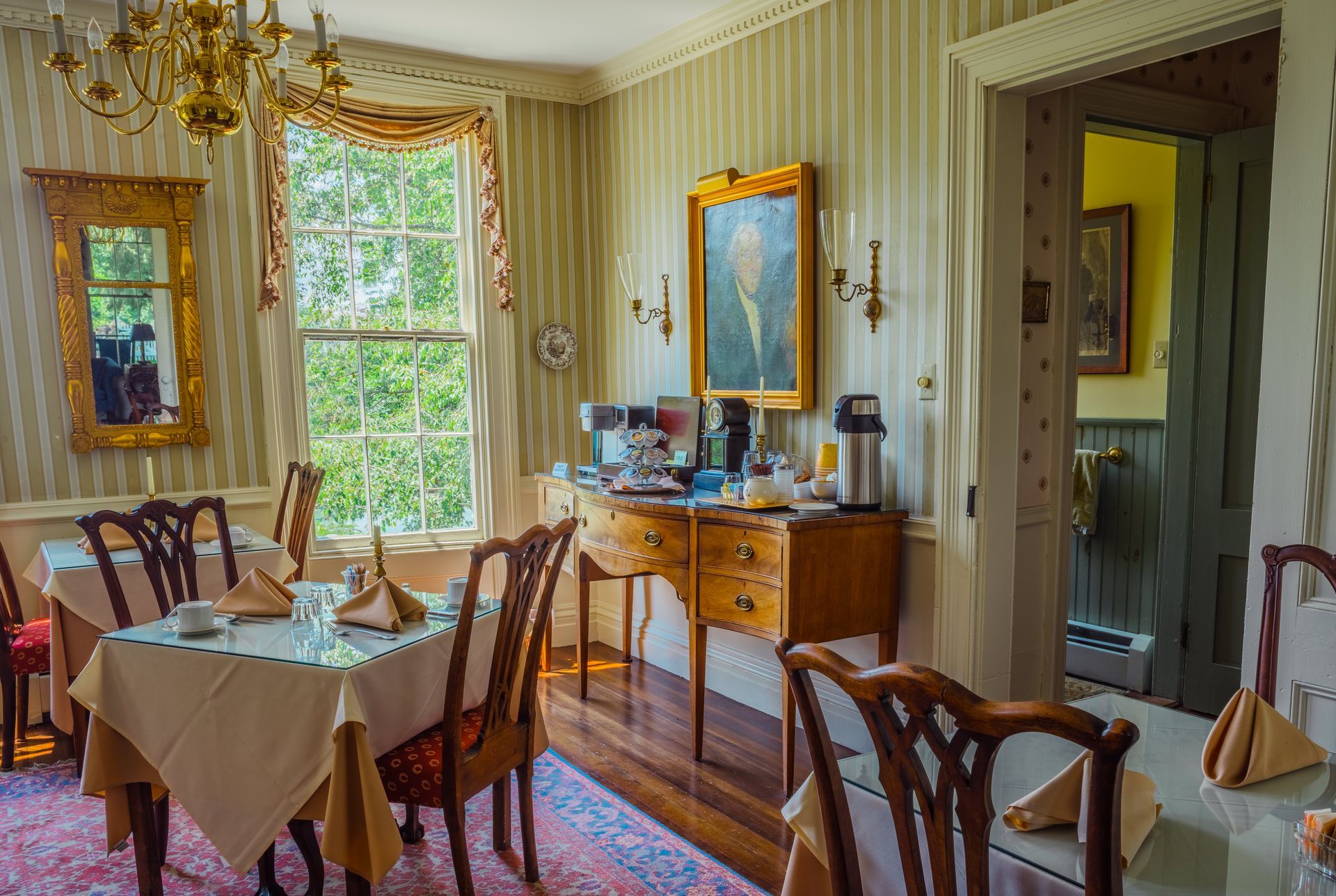 Dining room with table settings, antique furniture, portrait, and doorway.