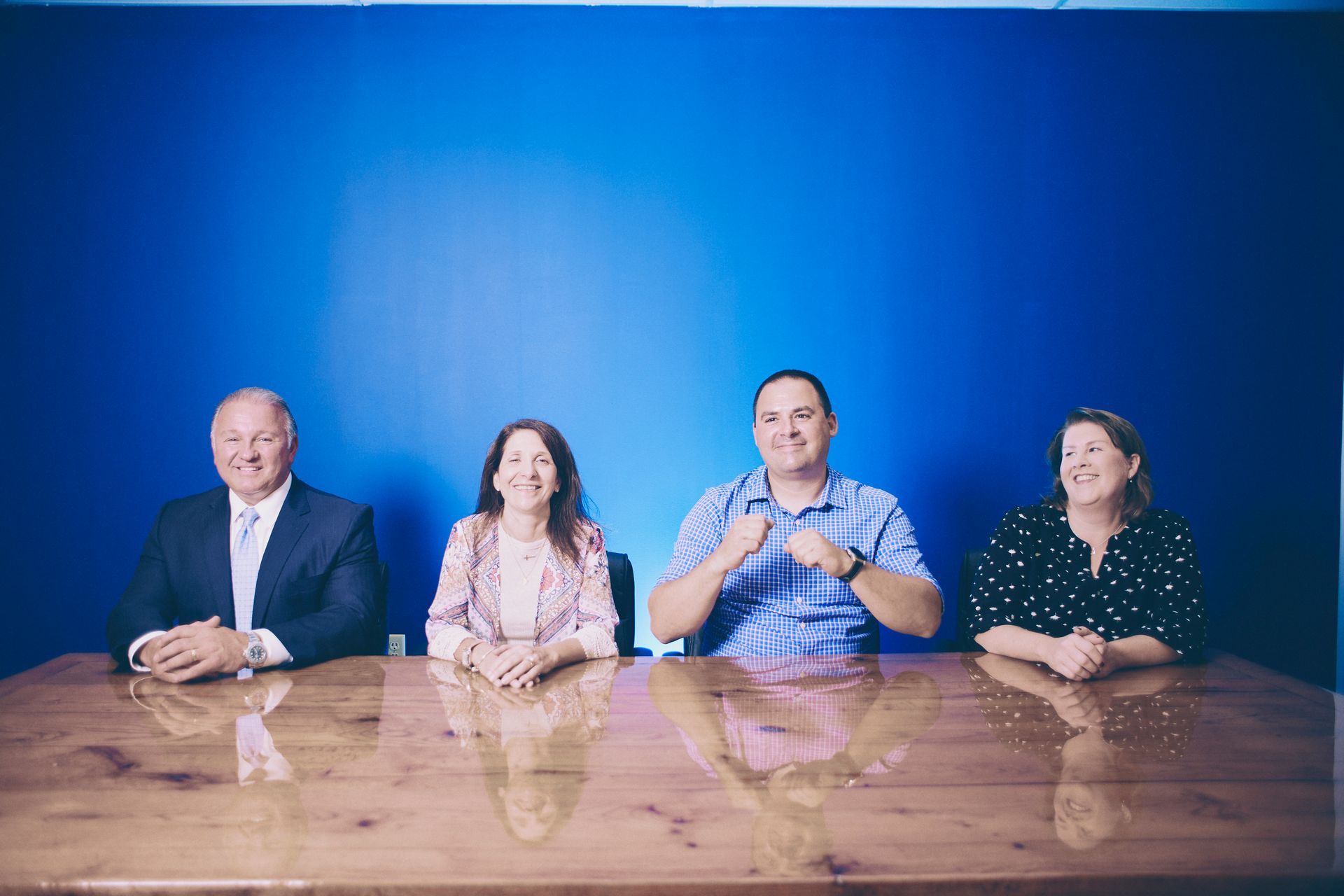 A group of people are sitting at a table in front of a blue wall.